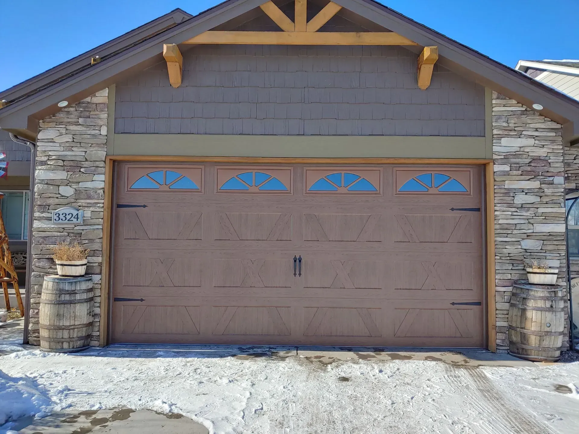Brown garage door with arched windows, flanked by stone columns, set in snow.
