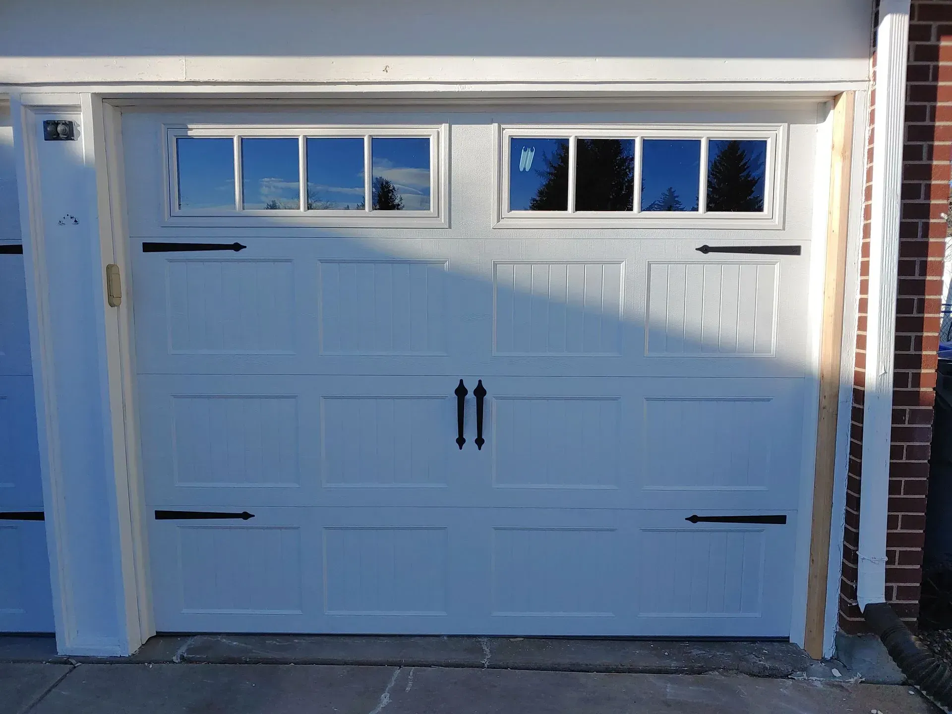 White garage door with windows, decorative hardware, and brick exterior.