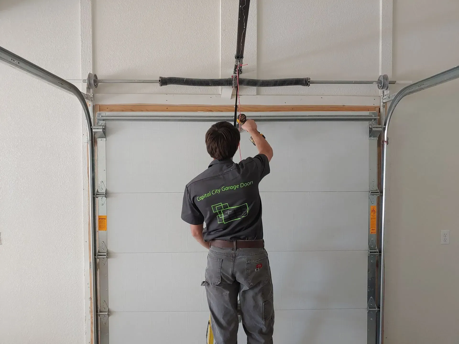 Garage door repairman adjusting a spring, standing inside a garage.