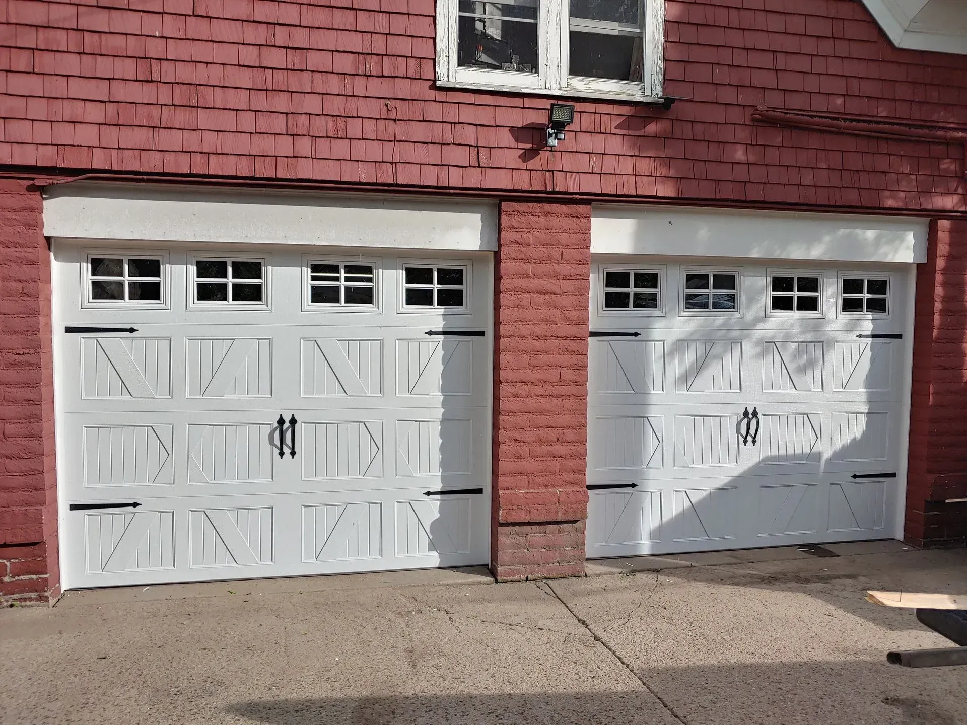 Two white garage doors with black hardware, red brick building exterior.