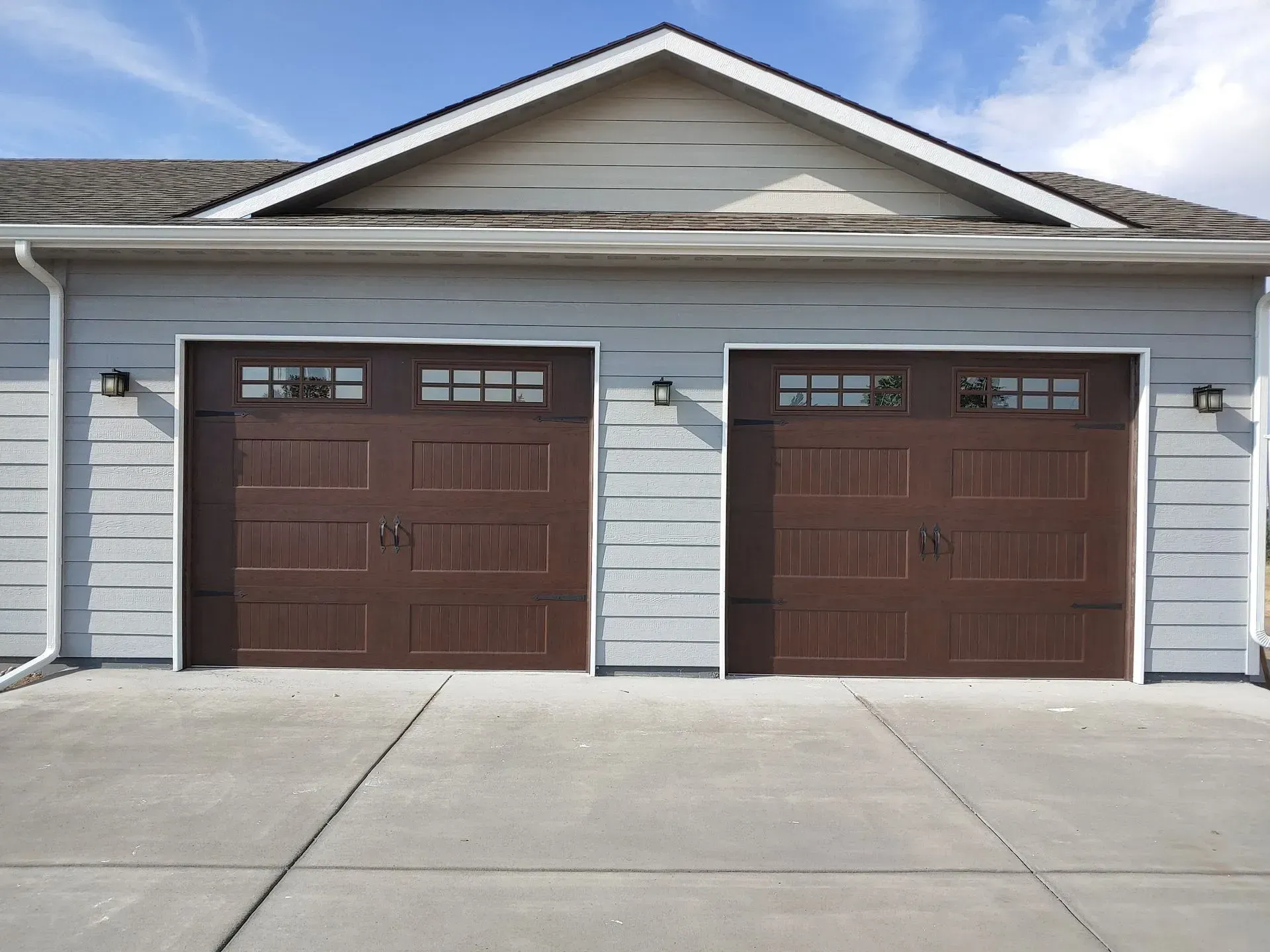 Two brown garage doors on a light blue building with a concrete driveway.