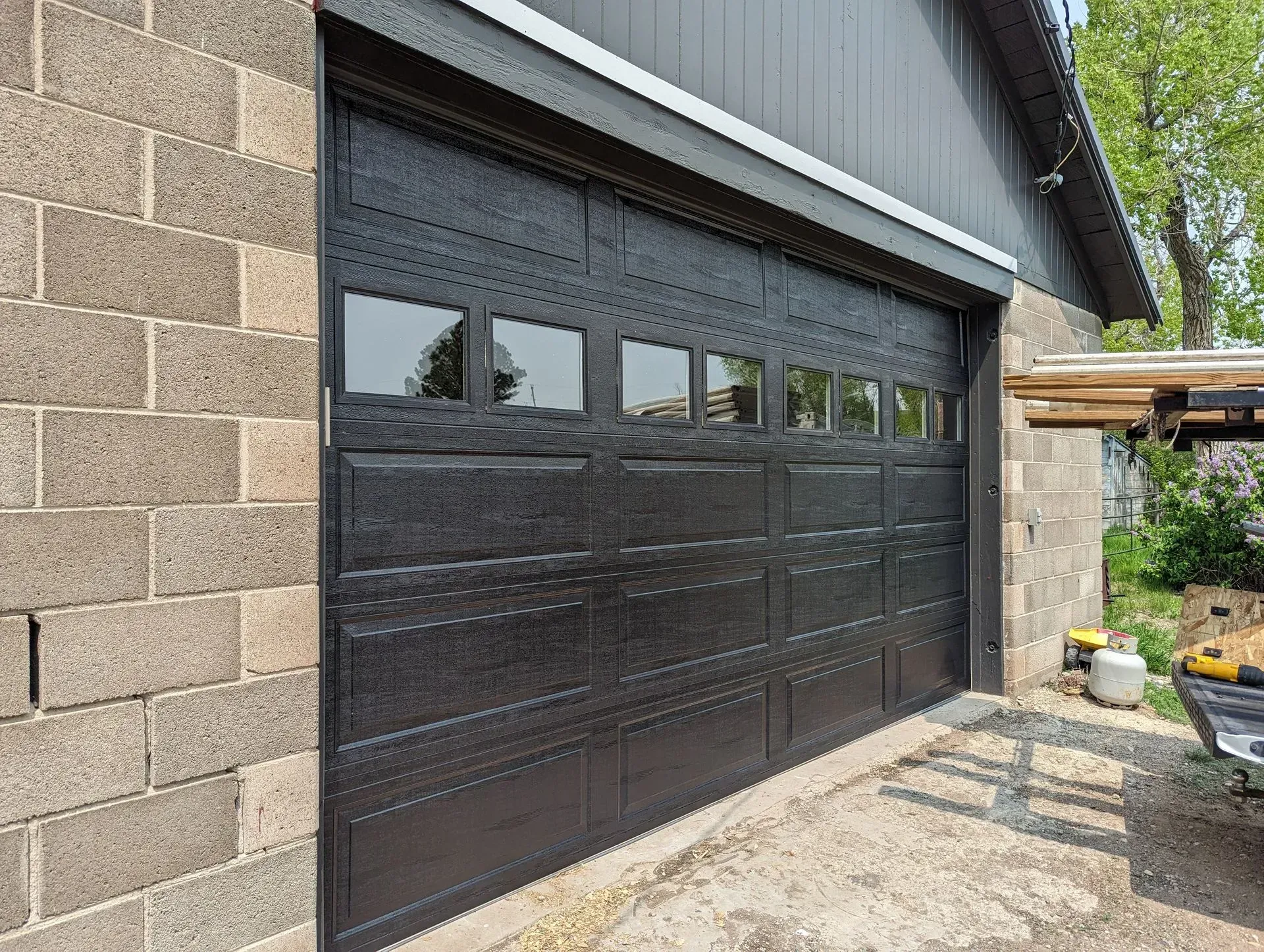 Black garage door with windows, set in a cinder block building.