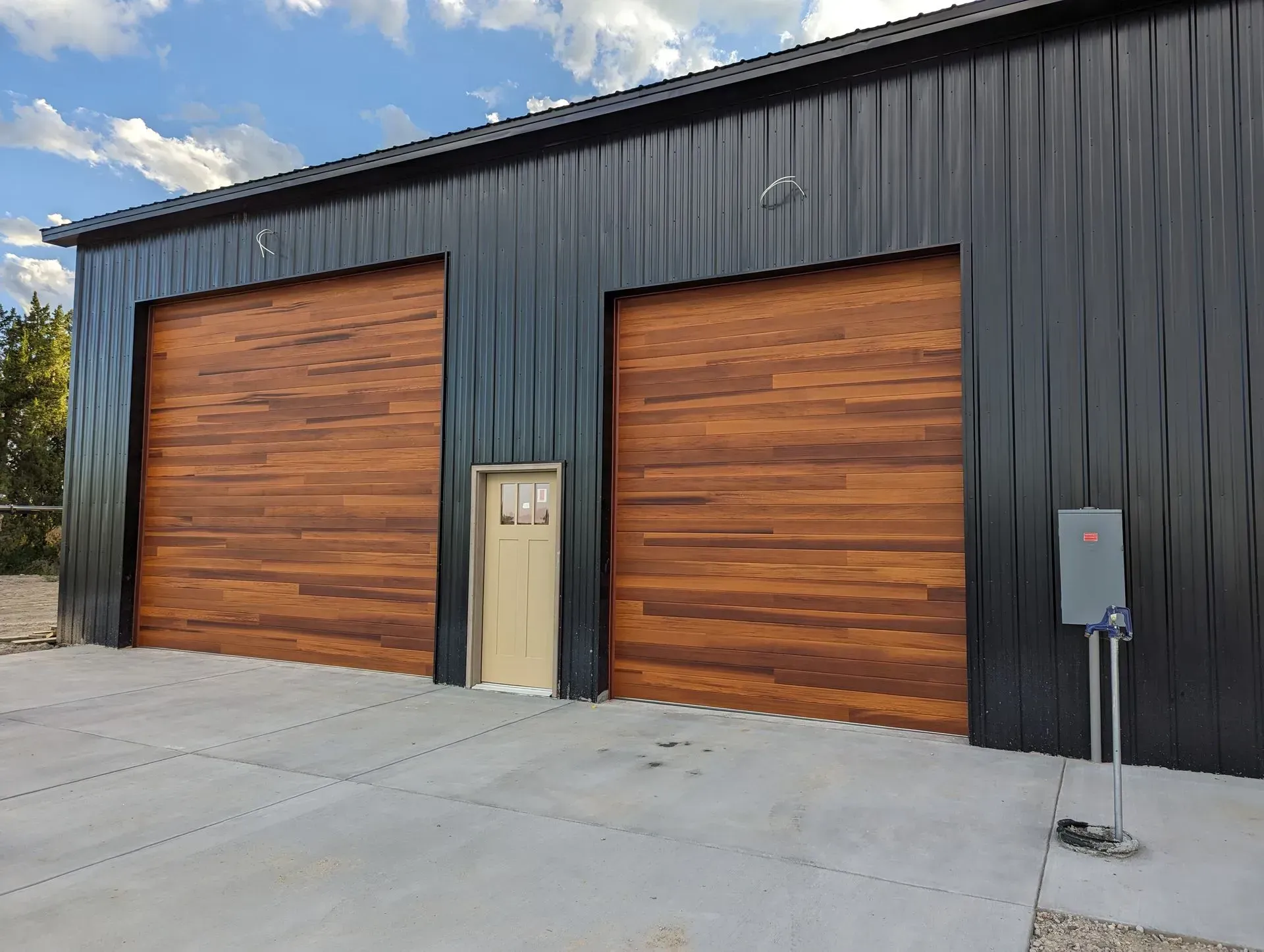 Black metal building with two brown wood garage doors and a tan door.