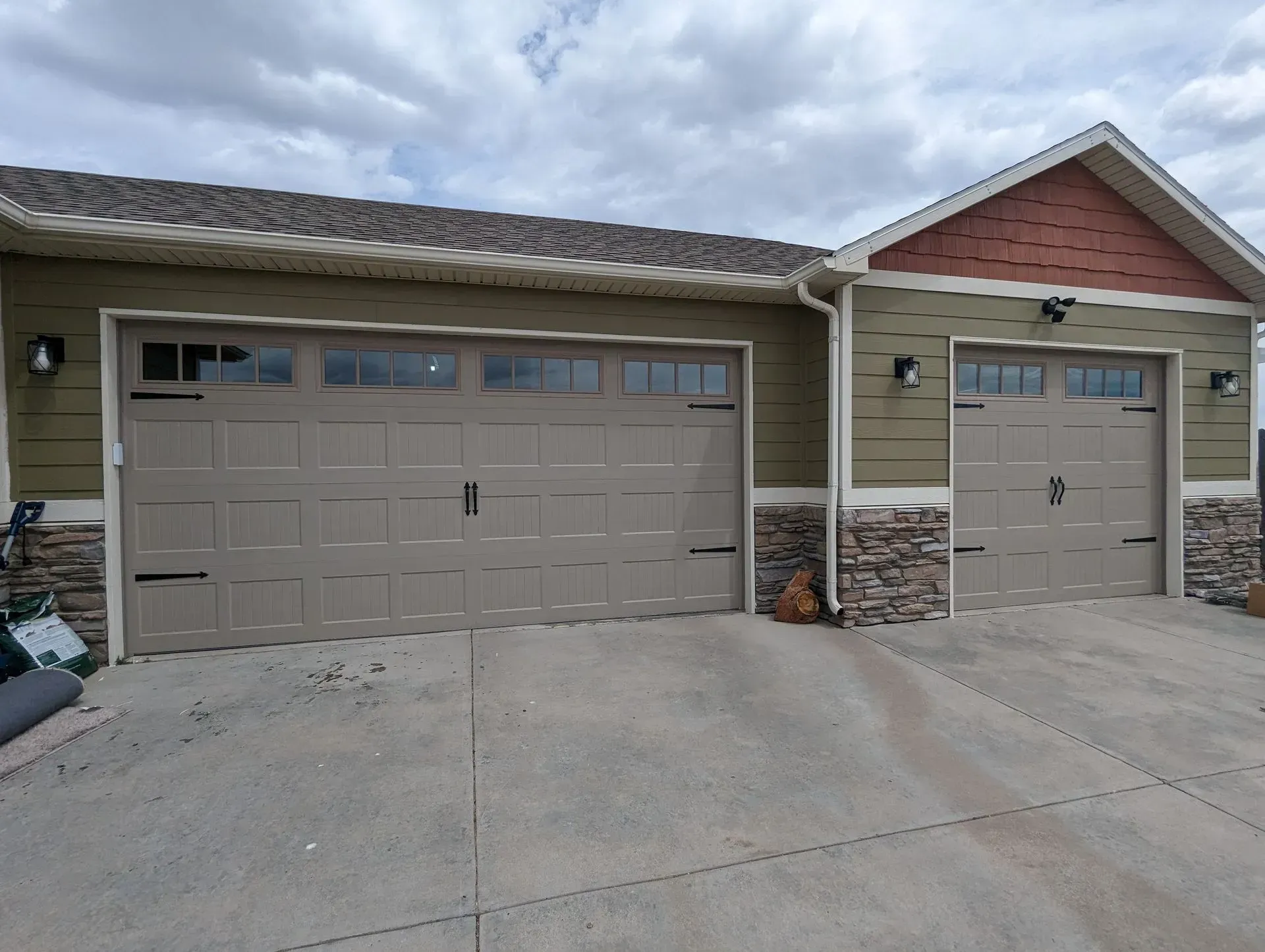 Tan garage doors on a green house with stone accents, under a cloudy sky.