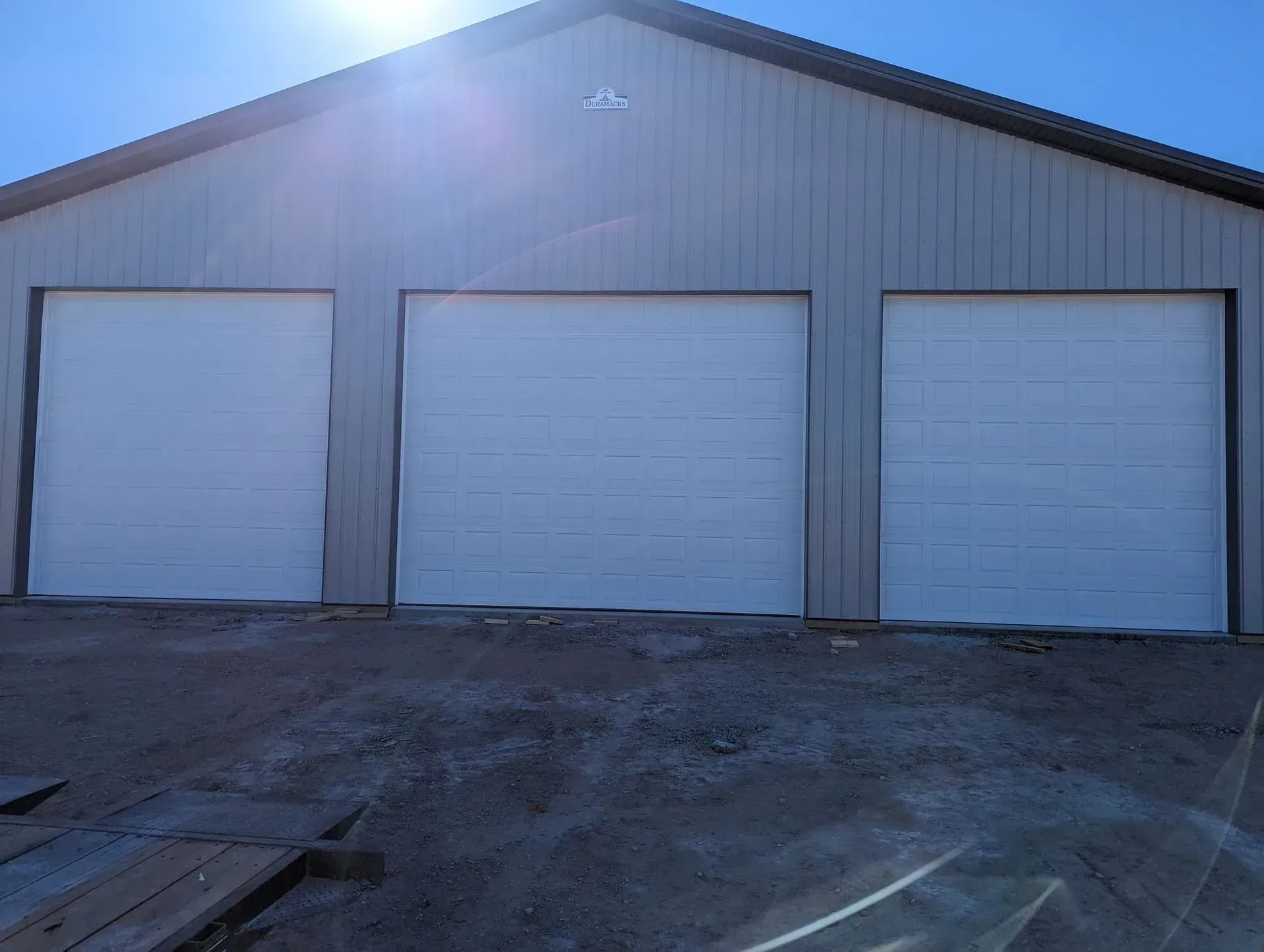 Three white garage doors on a light gray metal building under a bright sun.