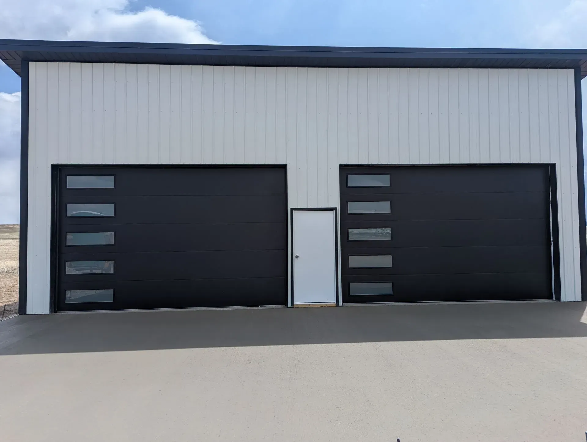 Two-bay garage with black doors and glass panels, white siding, and a small white door.
