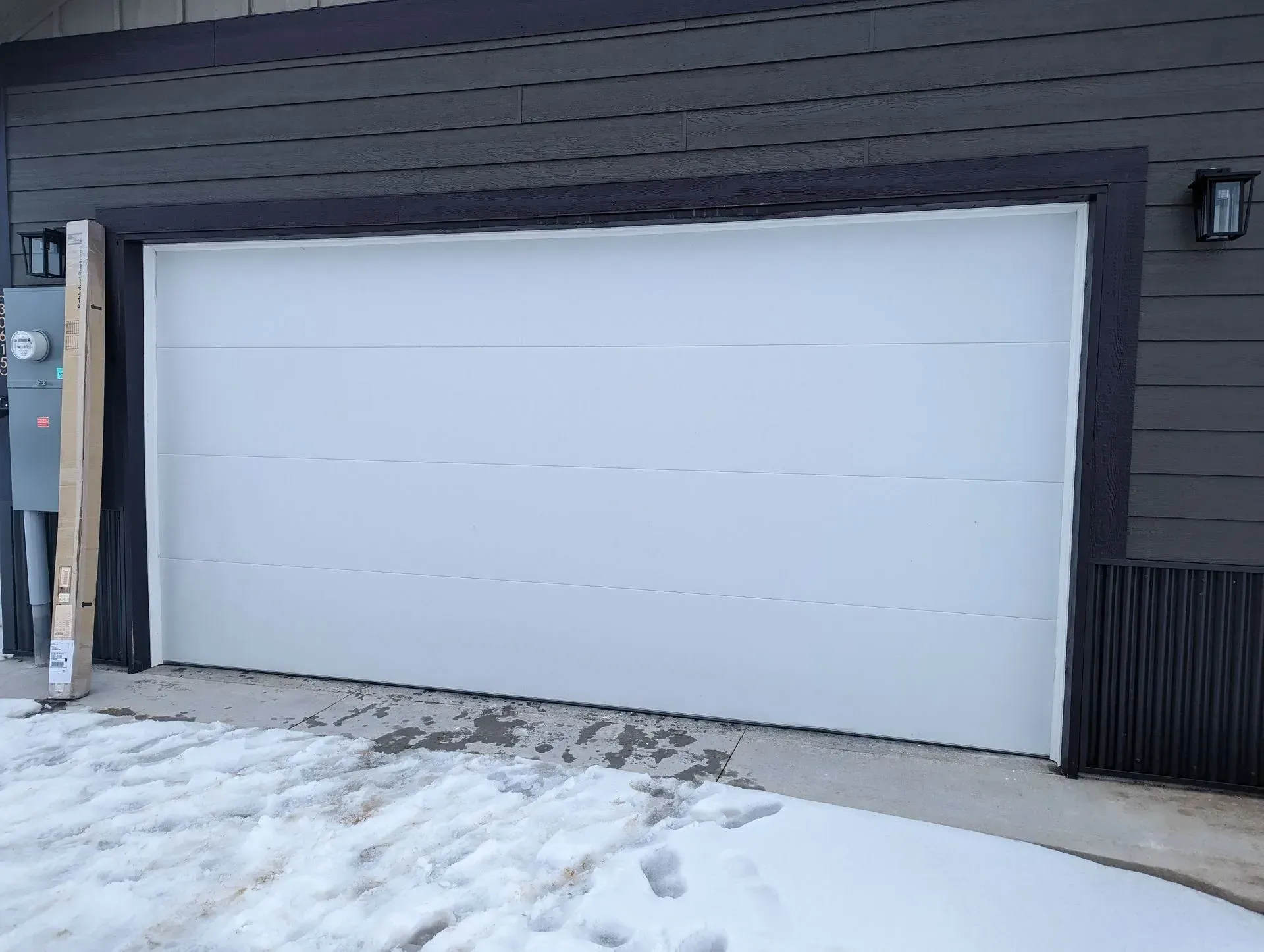 White garage door on a gray house, snow on the ground.