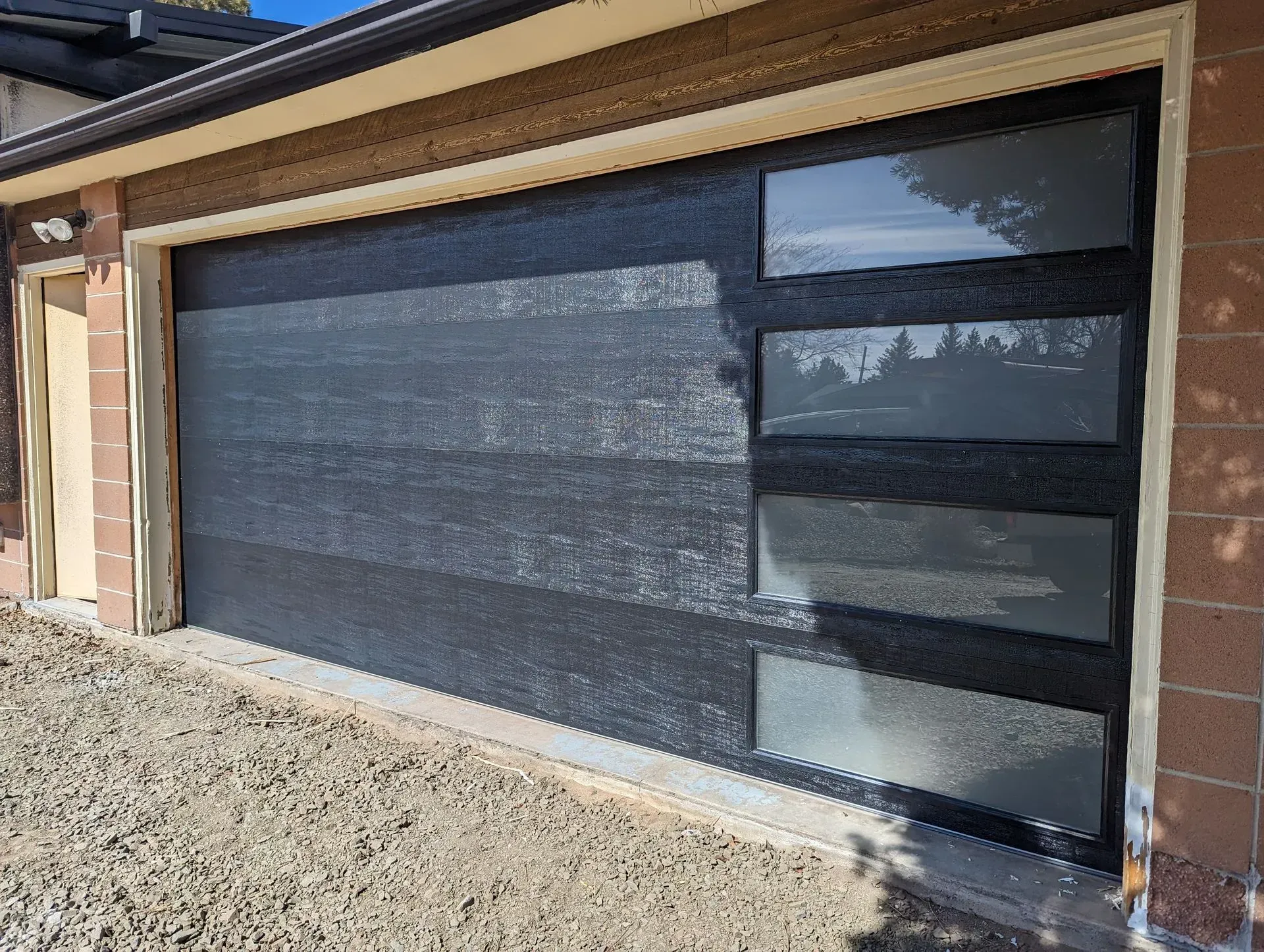 Modern black garage door with rectangular glass windows, set in a brick frame.