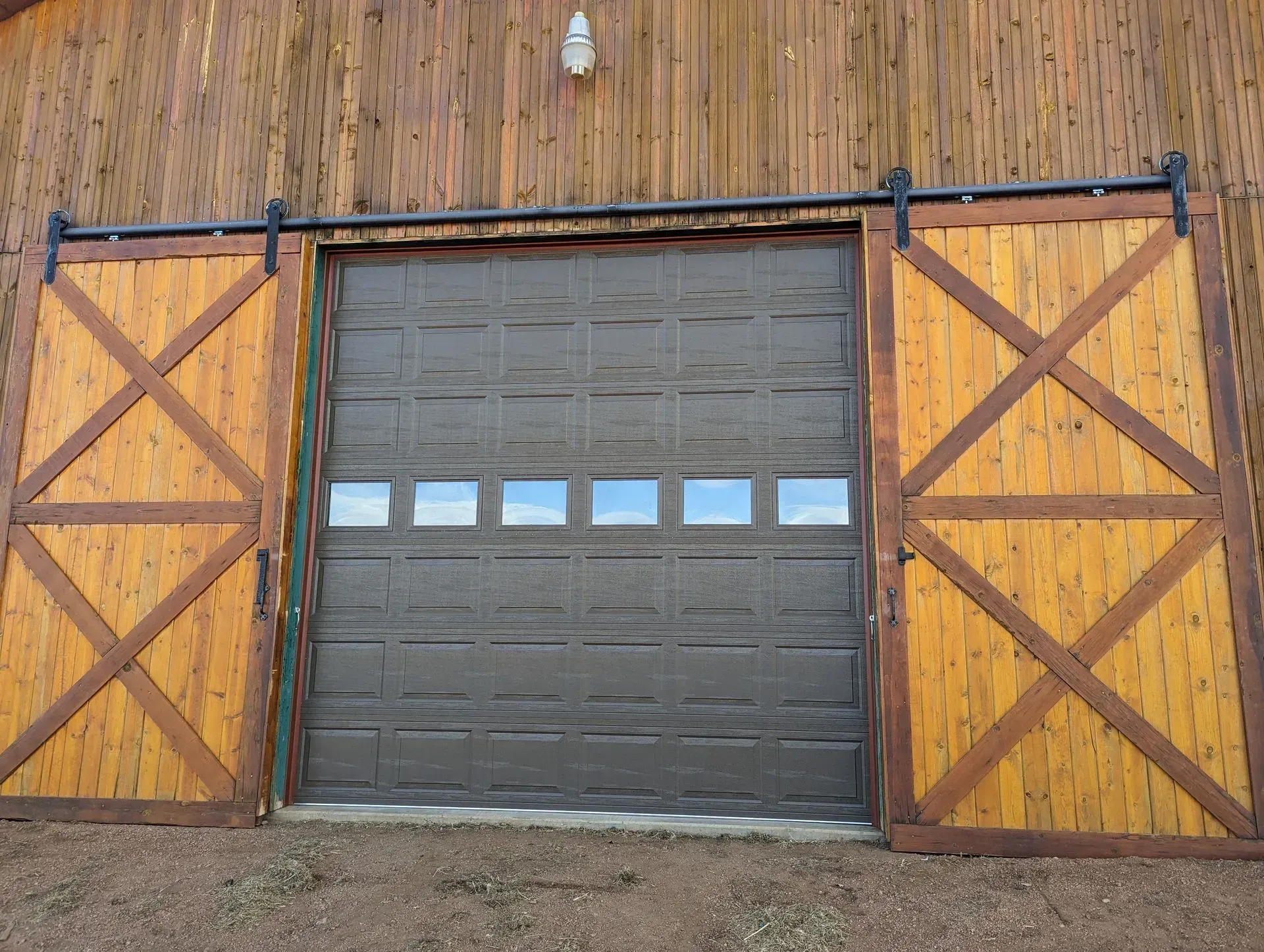 Garage with brown door, flanked by wooden sliding doors, mounted on a wooden building.
