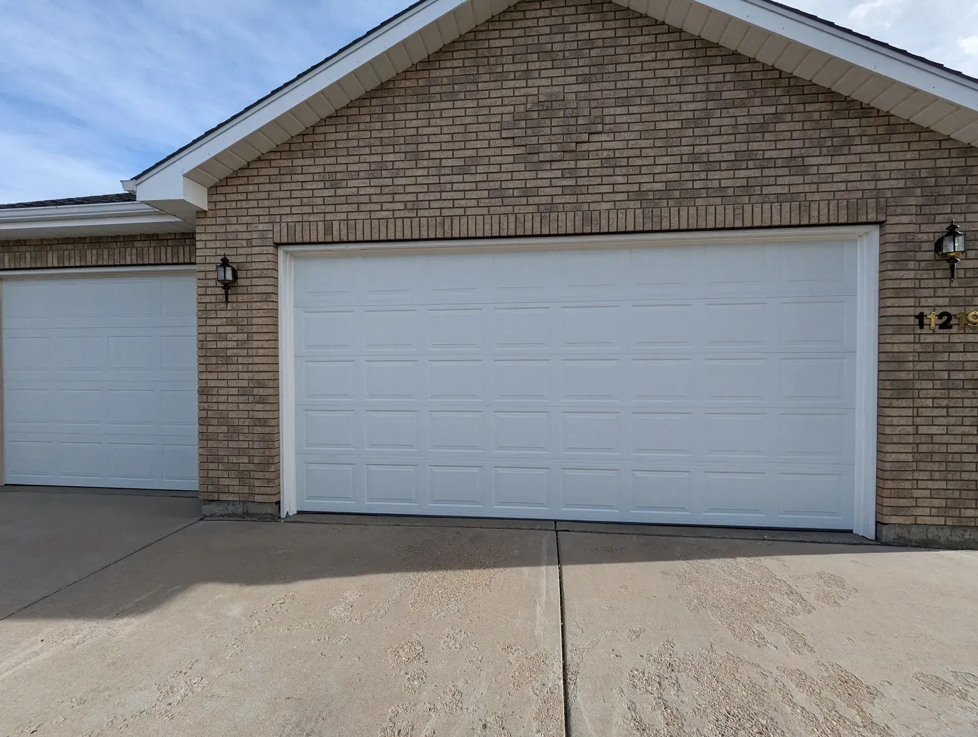 Two white garage doors on a brick house with concrete driveway, under a blue sky.