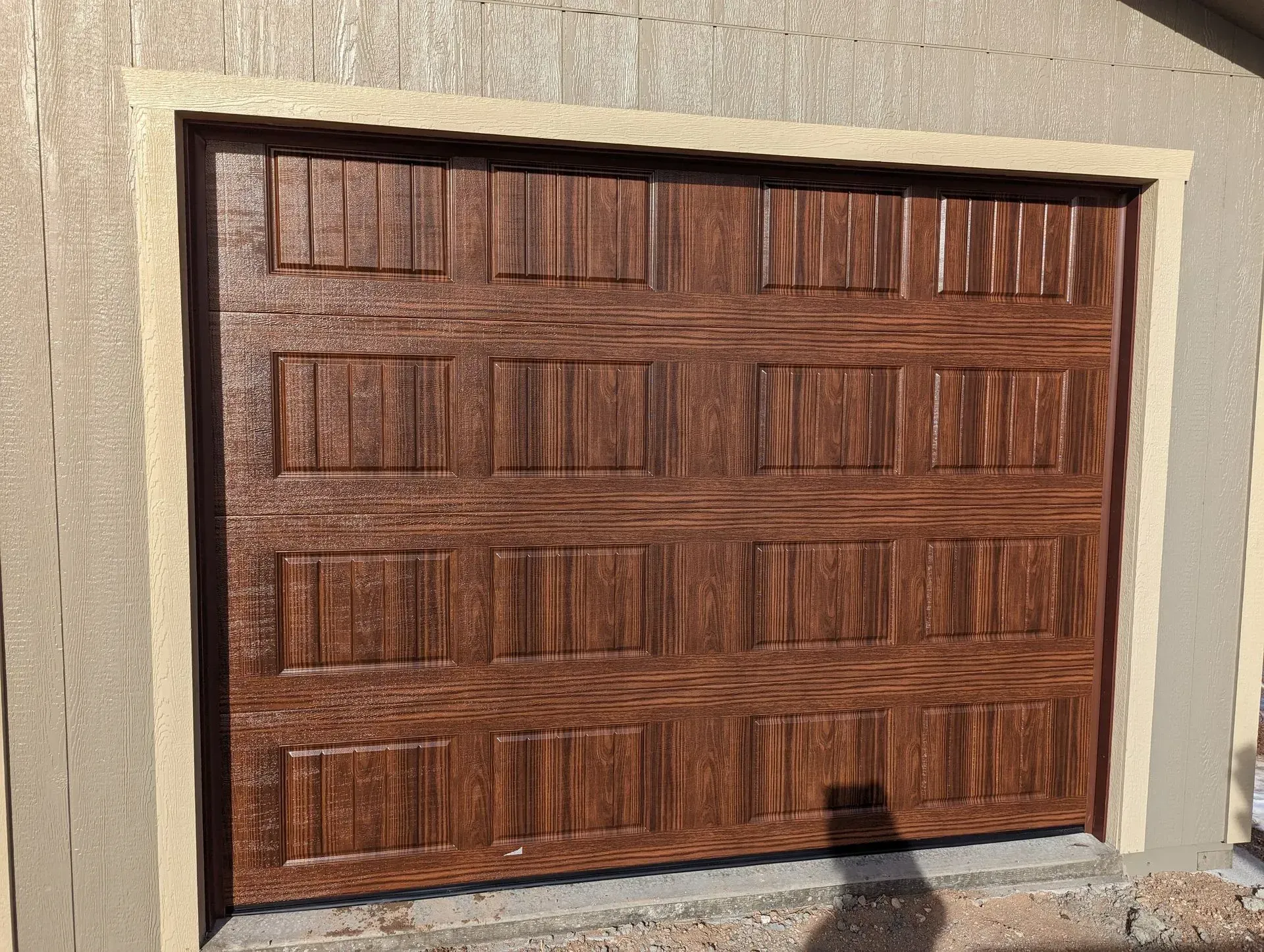 Brown wooden garage door with rectangular panels, set in a light beige frame.