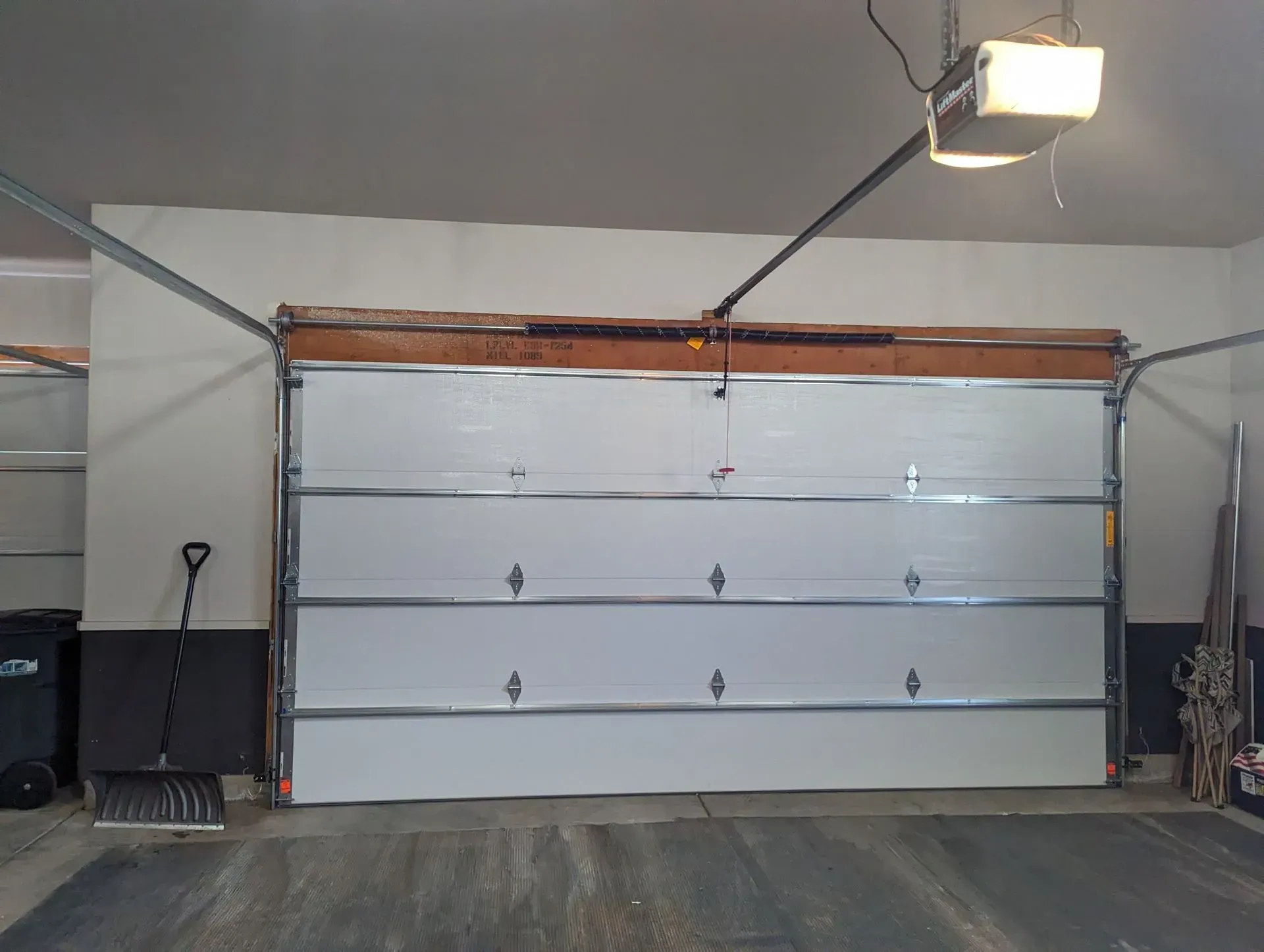 Garage interior with a closed white garage door, overhead light, and trash cans.