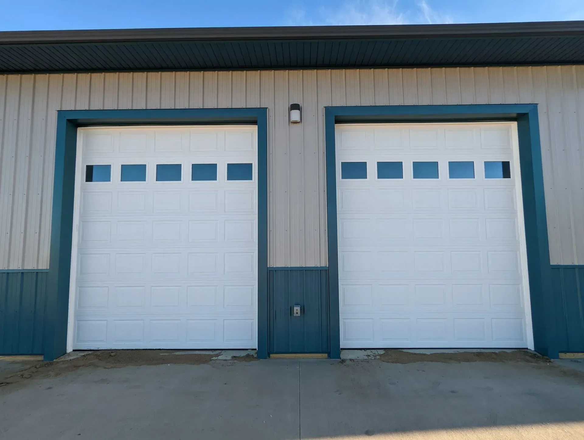 Two white garage doors with blue trim on a building under a blue sky.