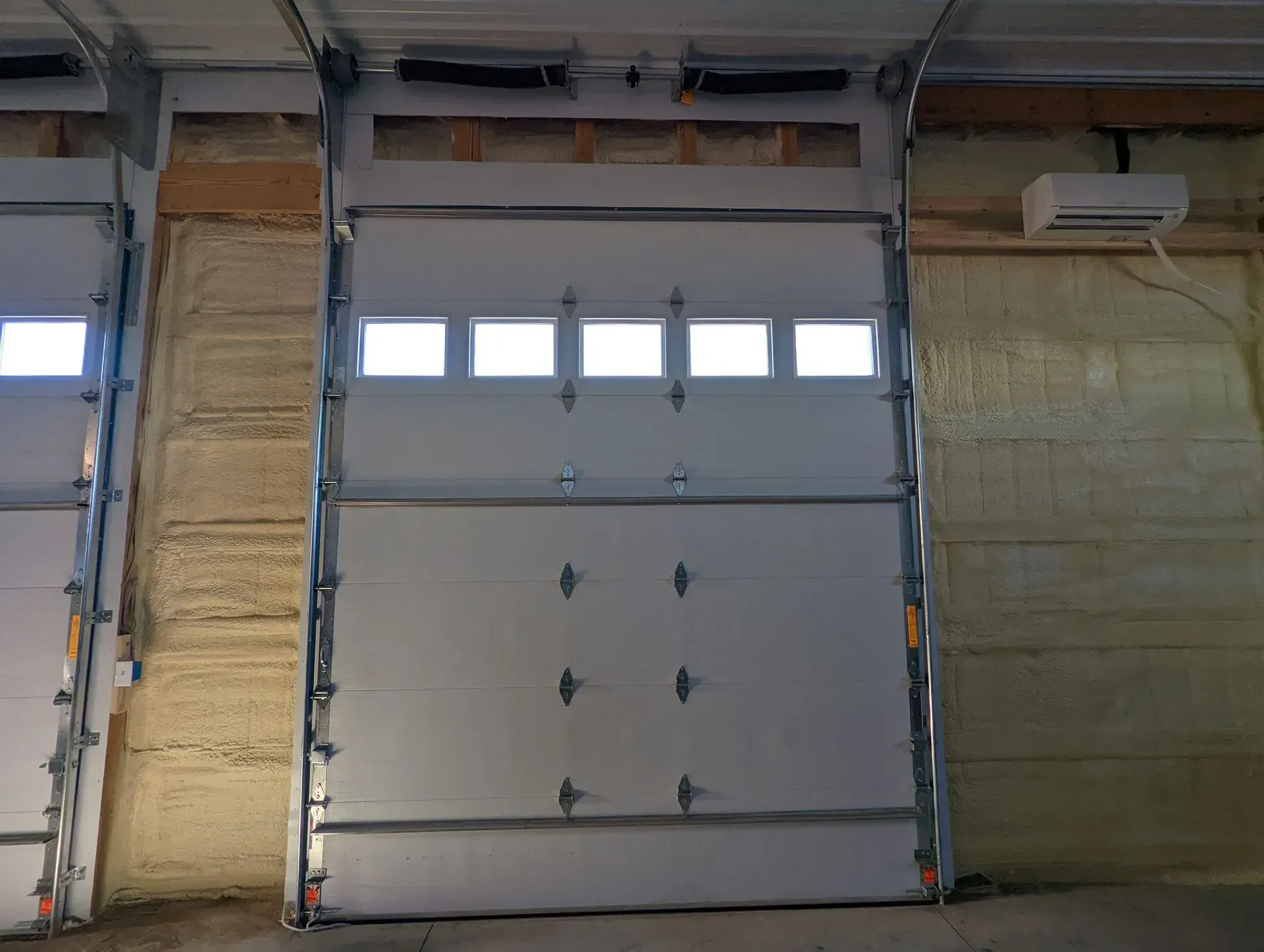 White garage door, windows at the top, inside a building with yellow insulation on the walls.
