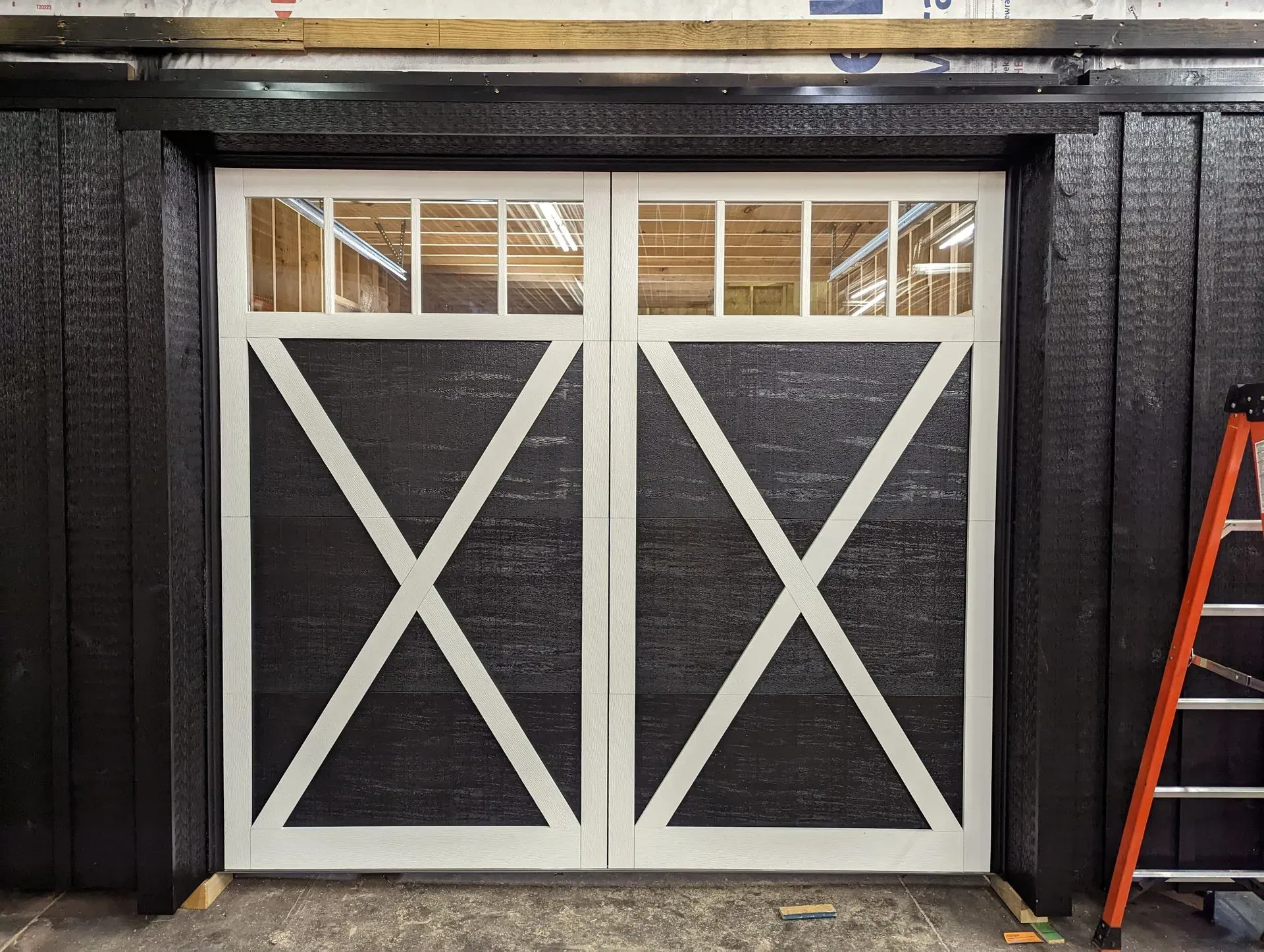 Black double barn doors with white X accents and glass panels, set in a black frame.