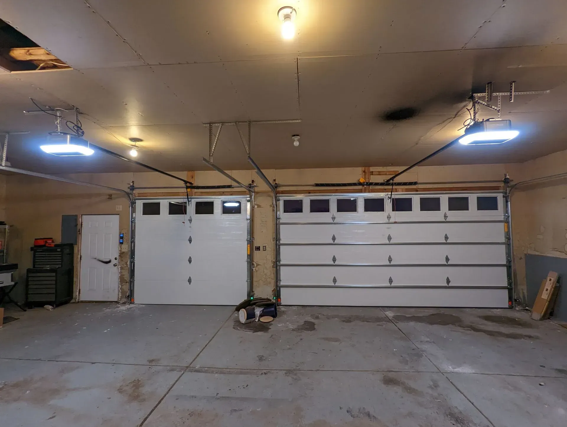 Garage interior with two white garage doors and overhead lighting.