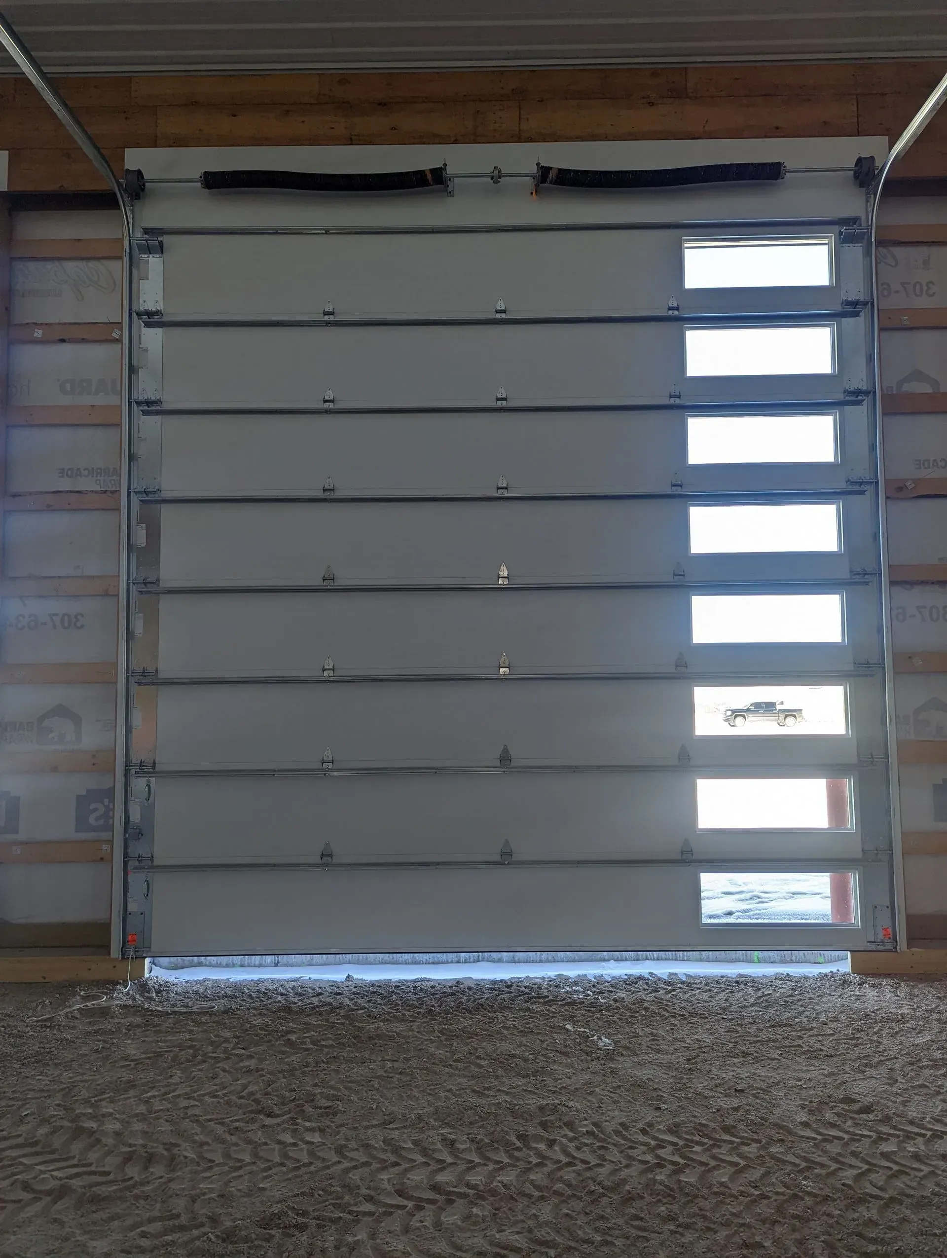 White metal overhead garage door with multiple horizontal panels and rectangular windows.
