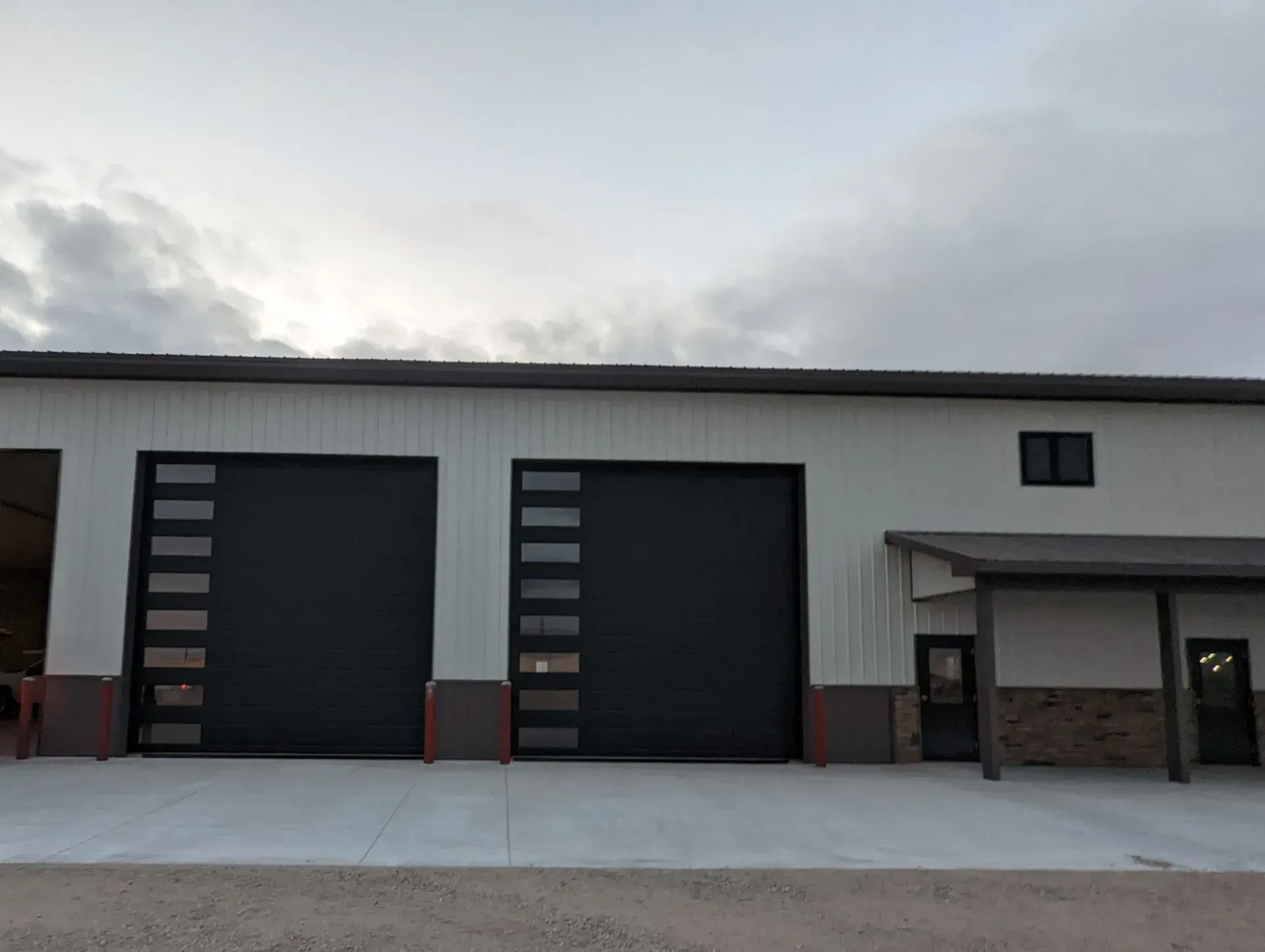 Exterior view of a commercial building with two black garage doors with windows, a white facade, and a covered entrance.