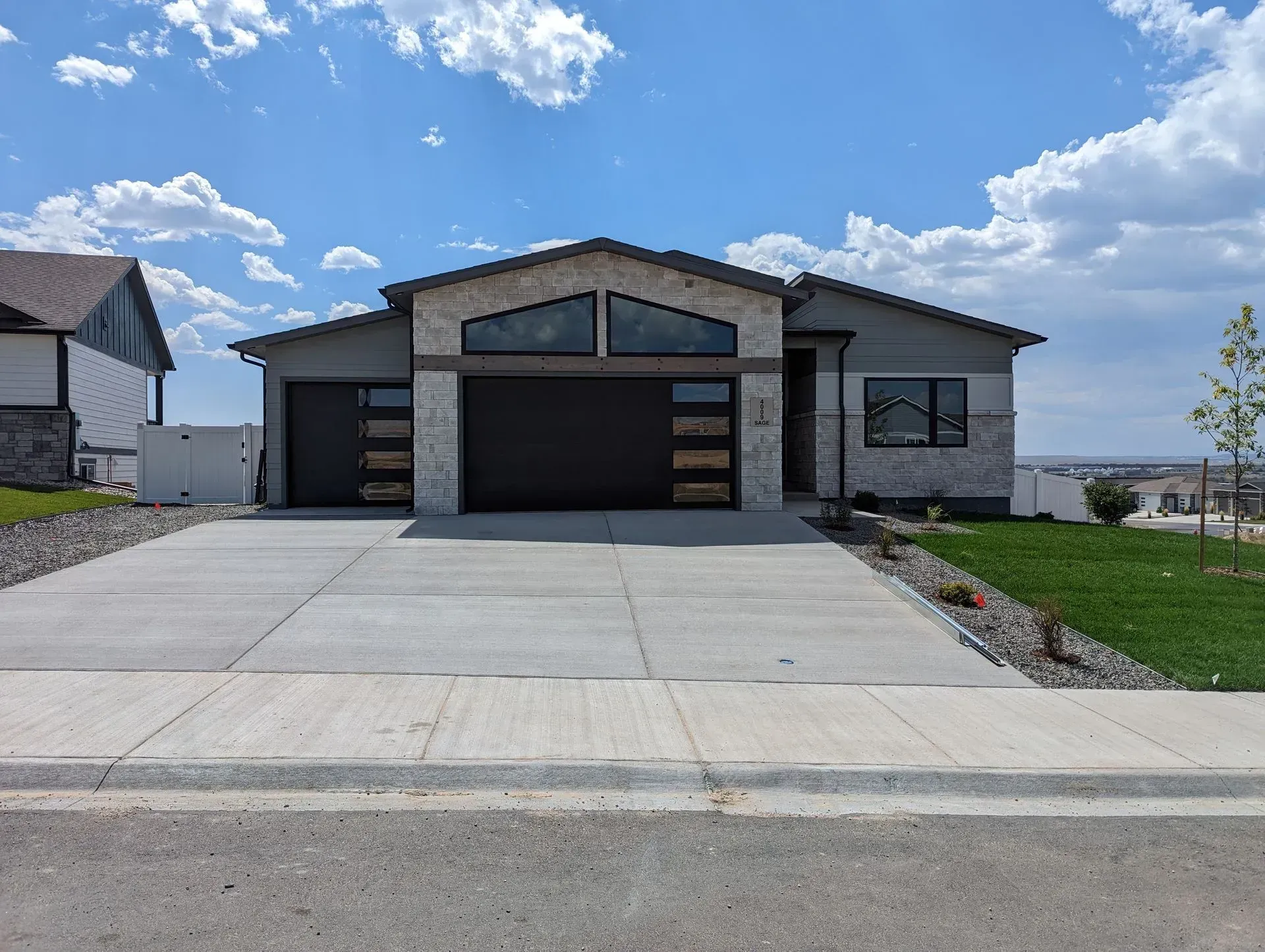 Modern single-story house with stone accents, a concrete driveway, and a blue sky.