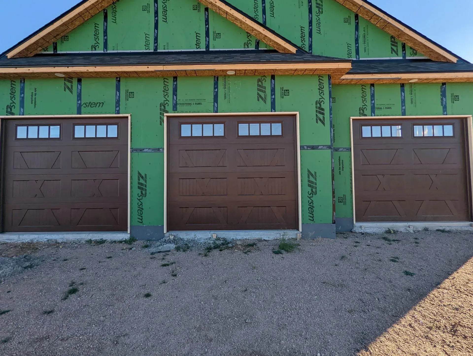 Three brown garage doors in a green-walled building, under construction.