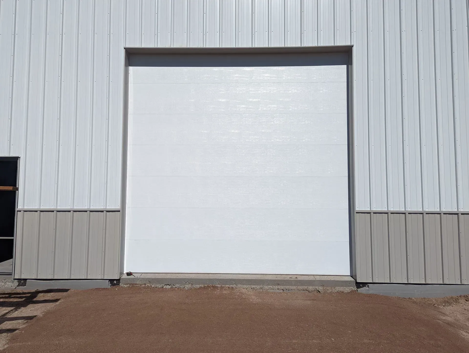 White overhead garage door on a metal building with a gravel ramp leading up to it.