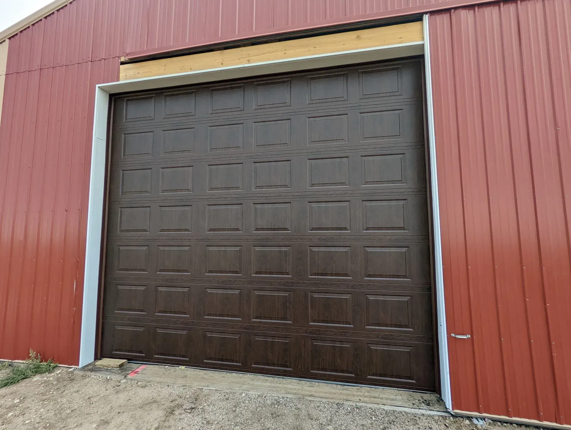 Brown garage door on a red metal building with white trim.