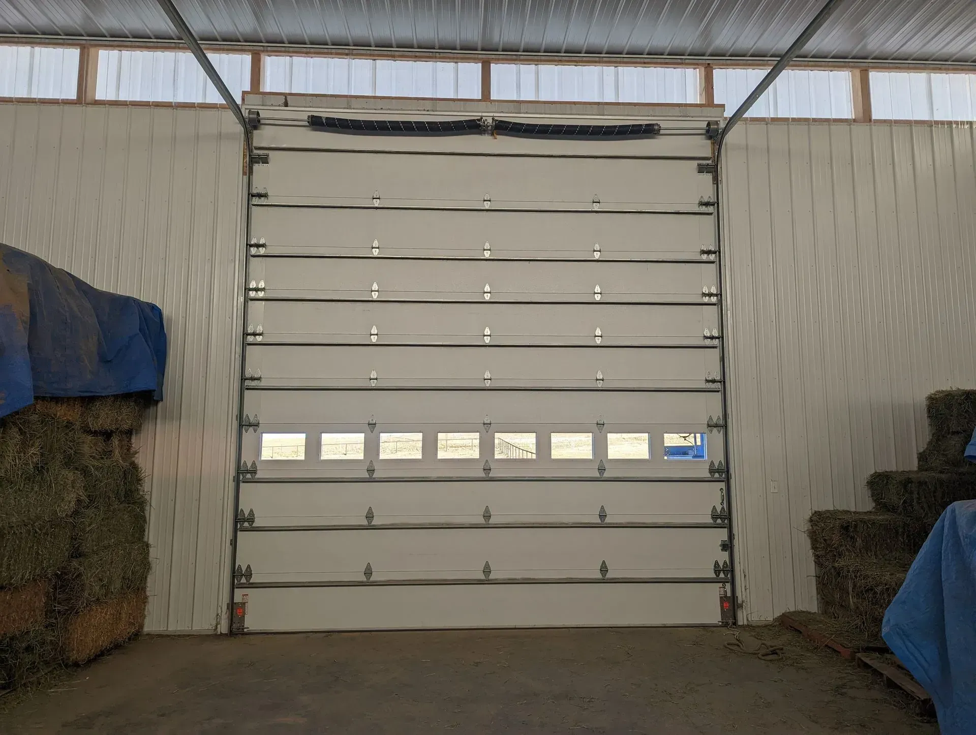 White closed overhead door in a barn. Hay bales on the left and right.