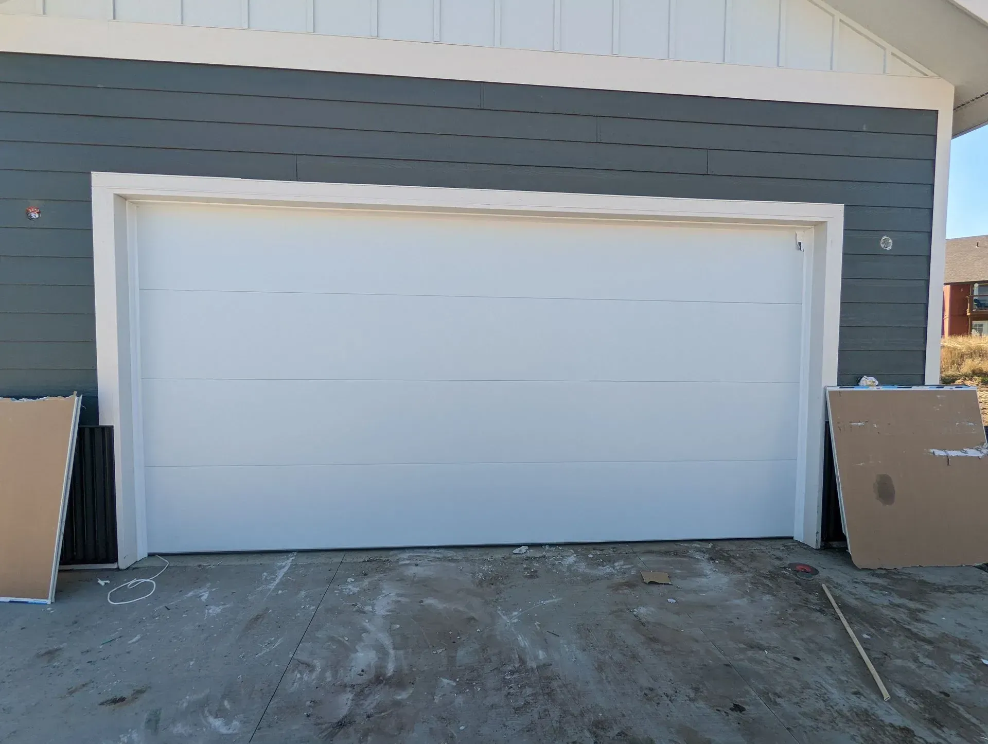 White garage door on a gray house with blue siding. Cardboard leaning against the sides.