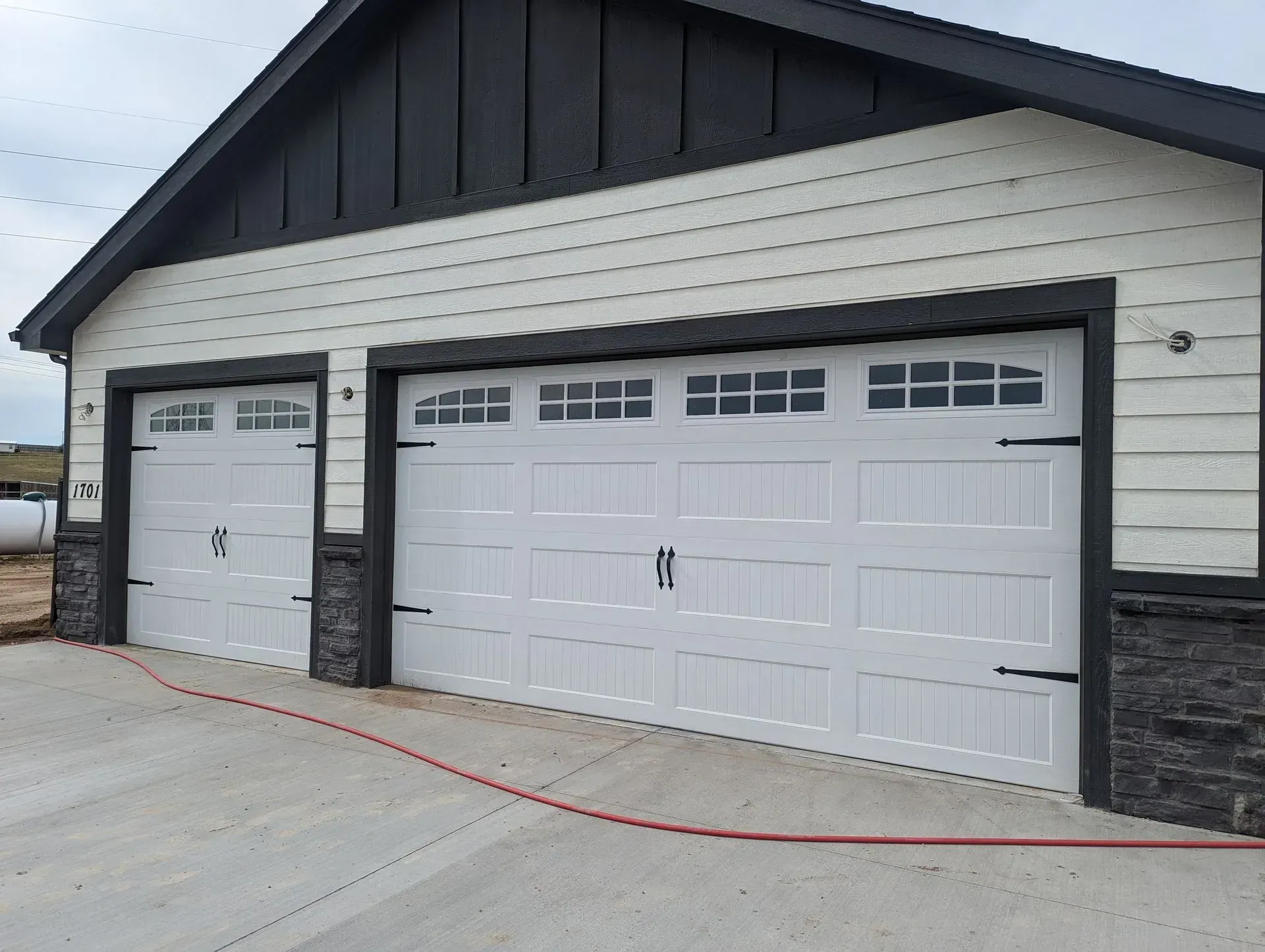 Two white garage doors on a light-colored house with black trim. Stone accents and a dark roof.