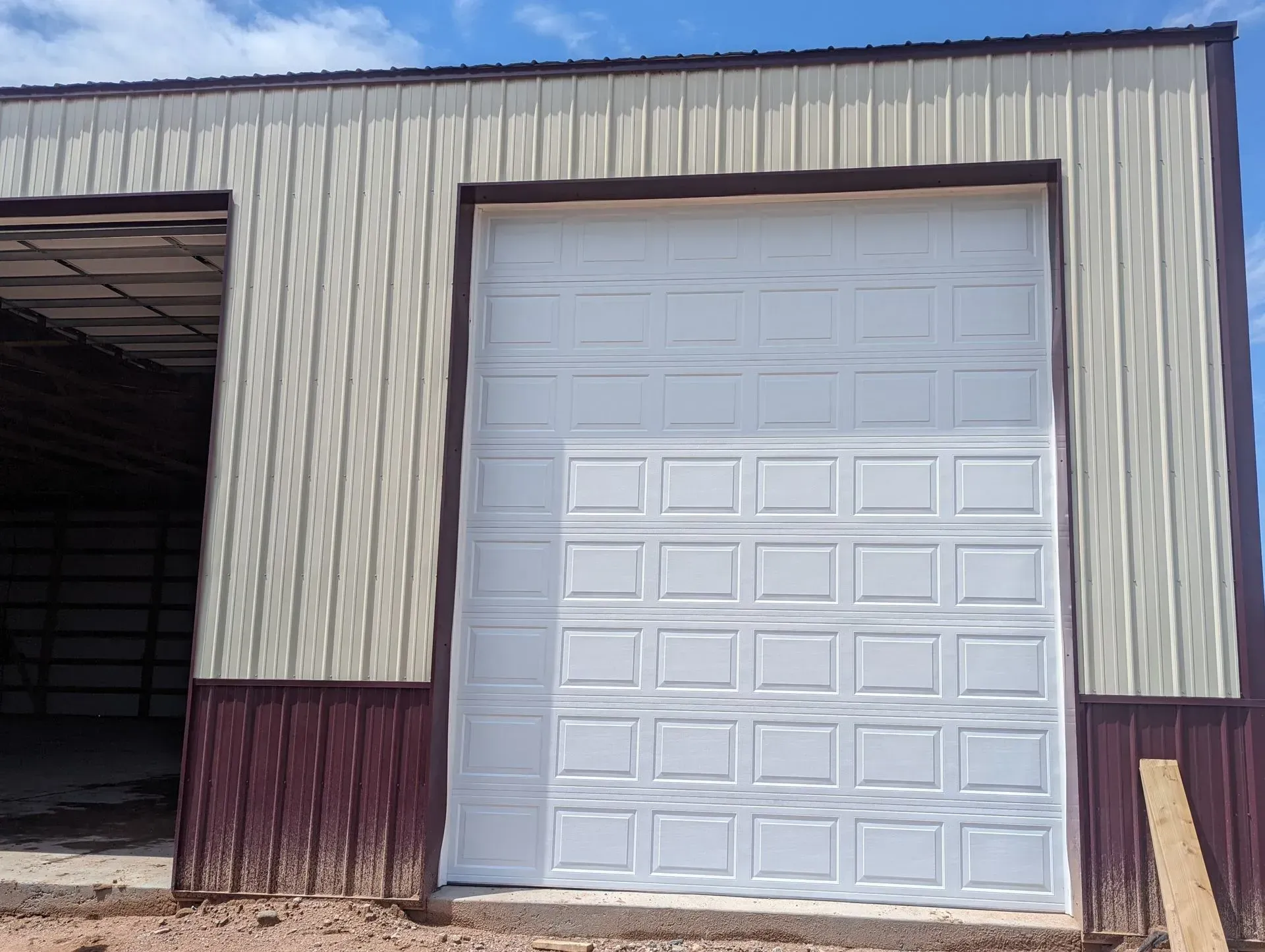 White garage door on a metal building with burgundy trim. Exterior setting, daytime.
