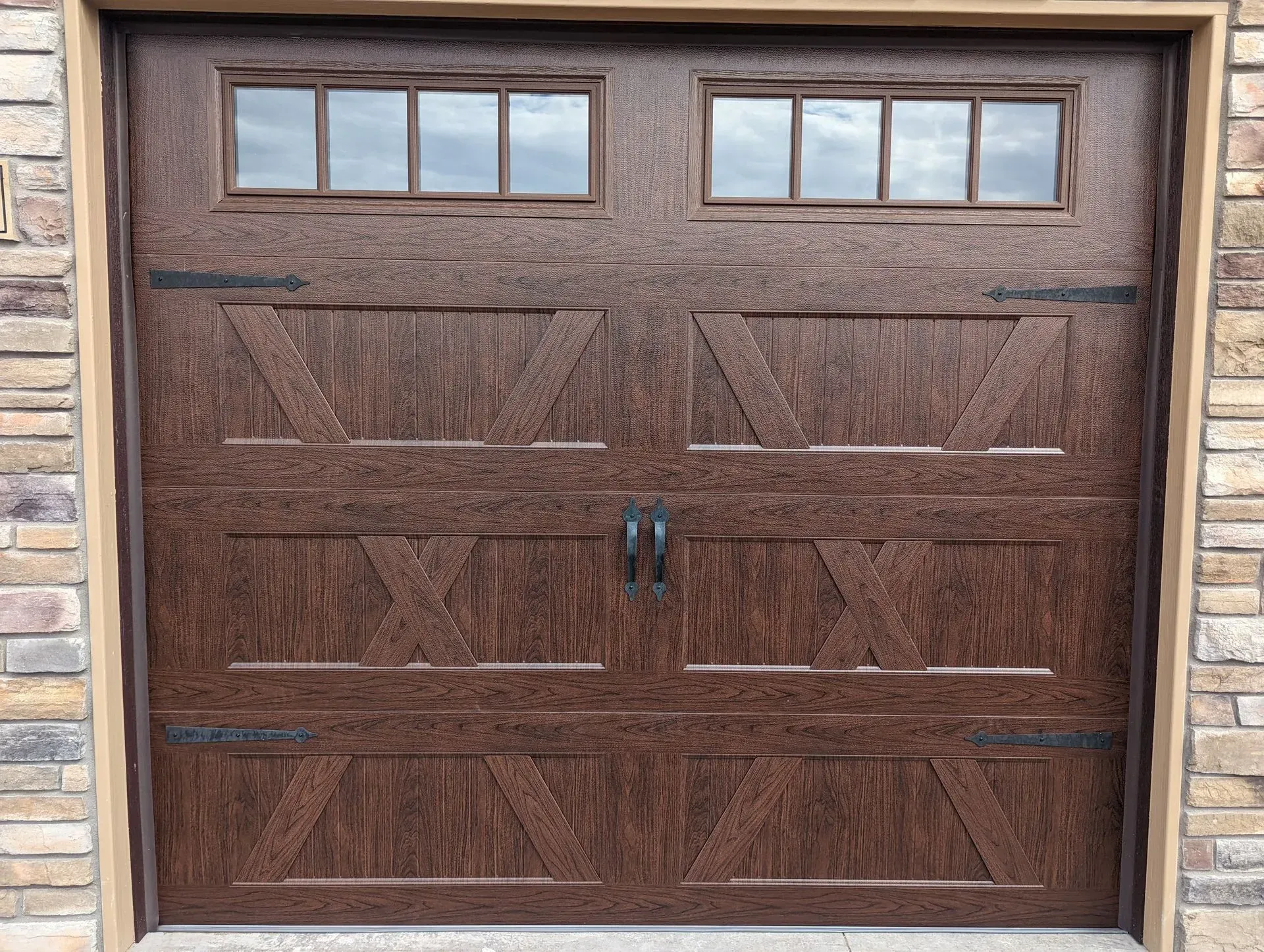 Brown garage door with windows, decorative hardware, set in a stone-trimmed frame.
