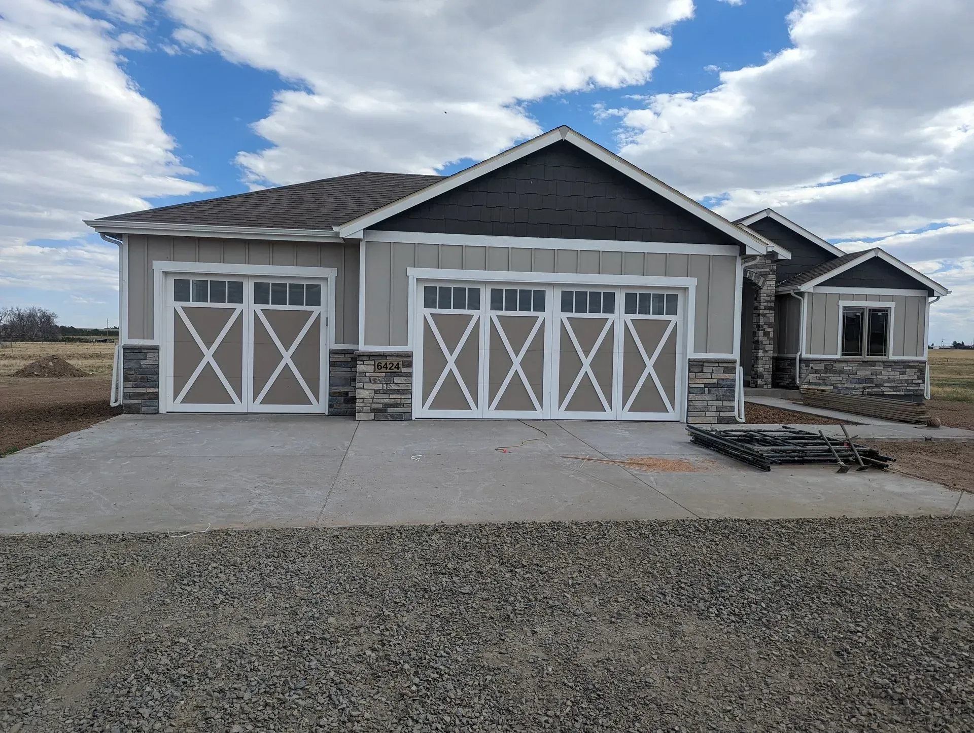Light gray house with stone accents, brown garage doors, and blue sky.