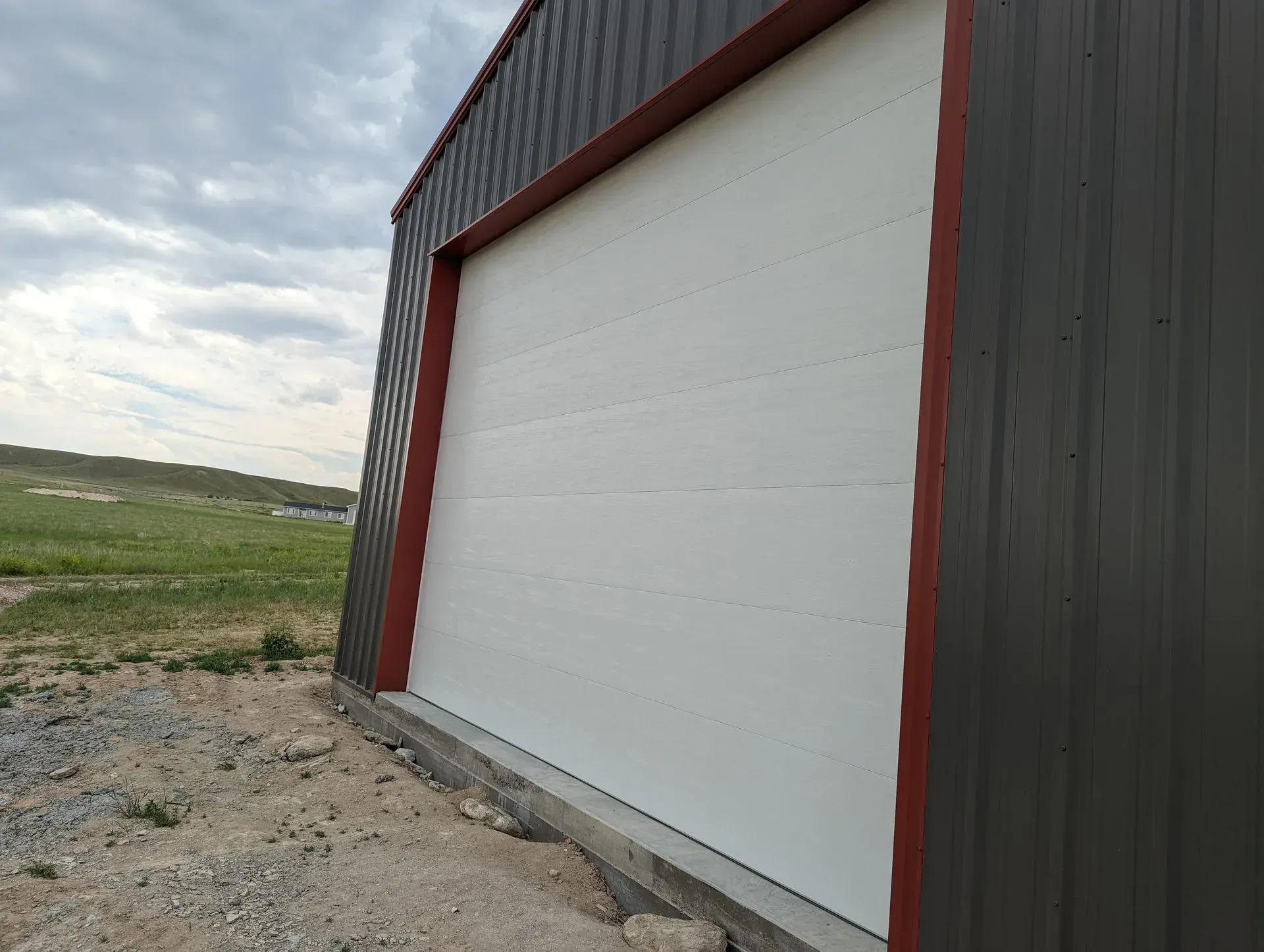 White overhead door on a gray metal building with a red frame, outdoors.