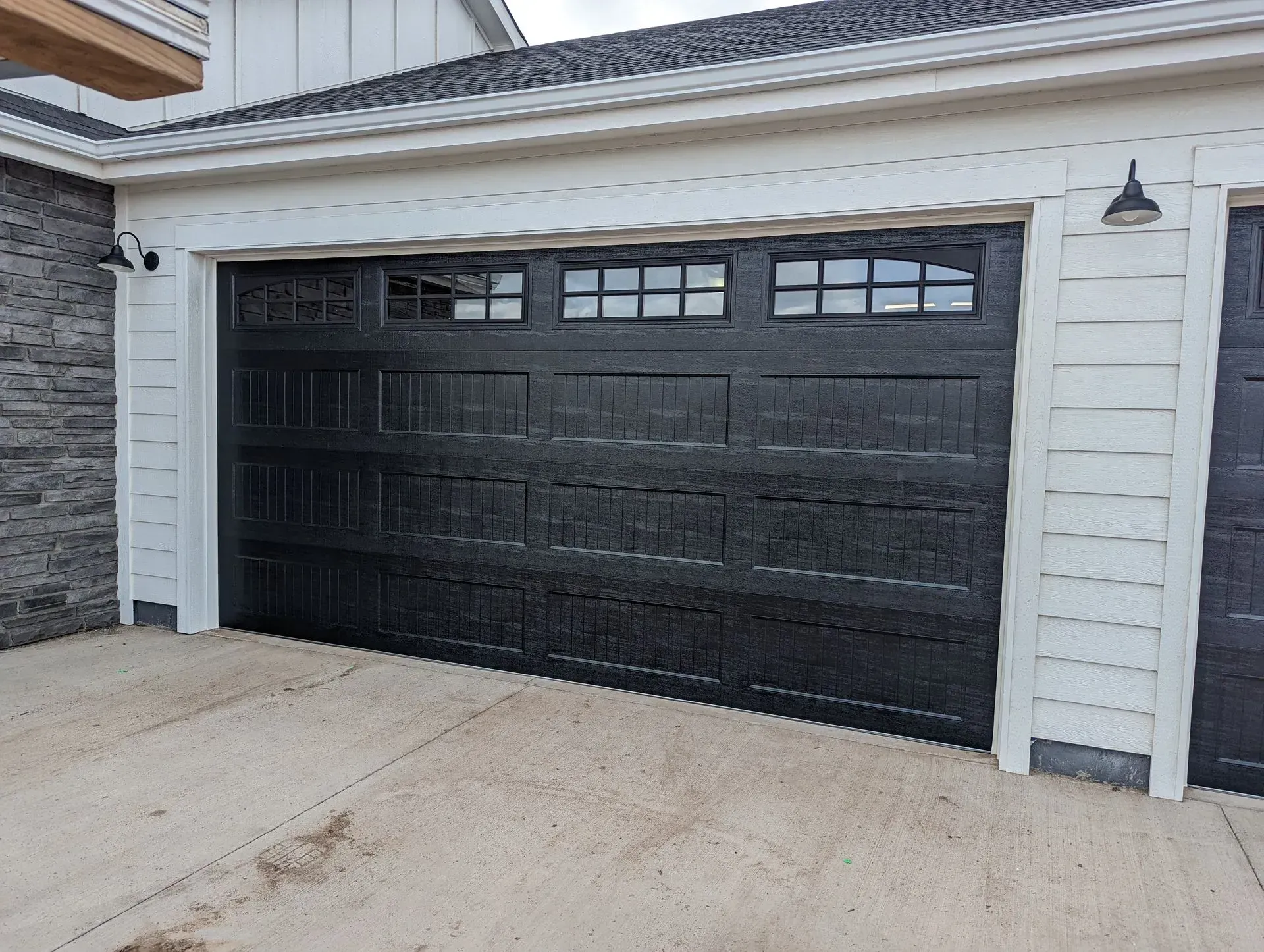 Black garage door with windows, white trim, and siding. Outdoor setting.