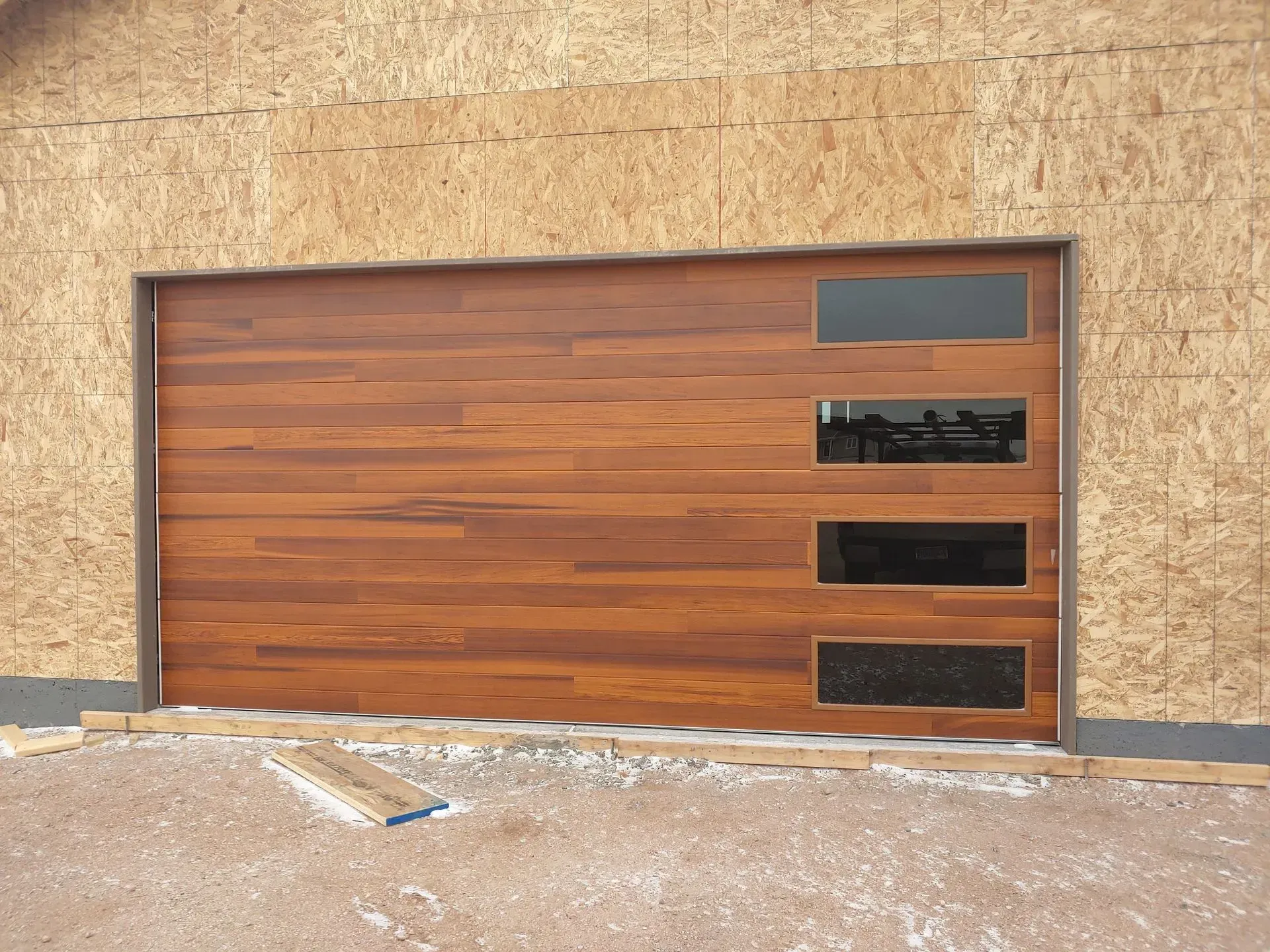 Wooden garage door with three rectangular windows, framed by unfinished wood siding.