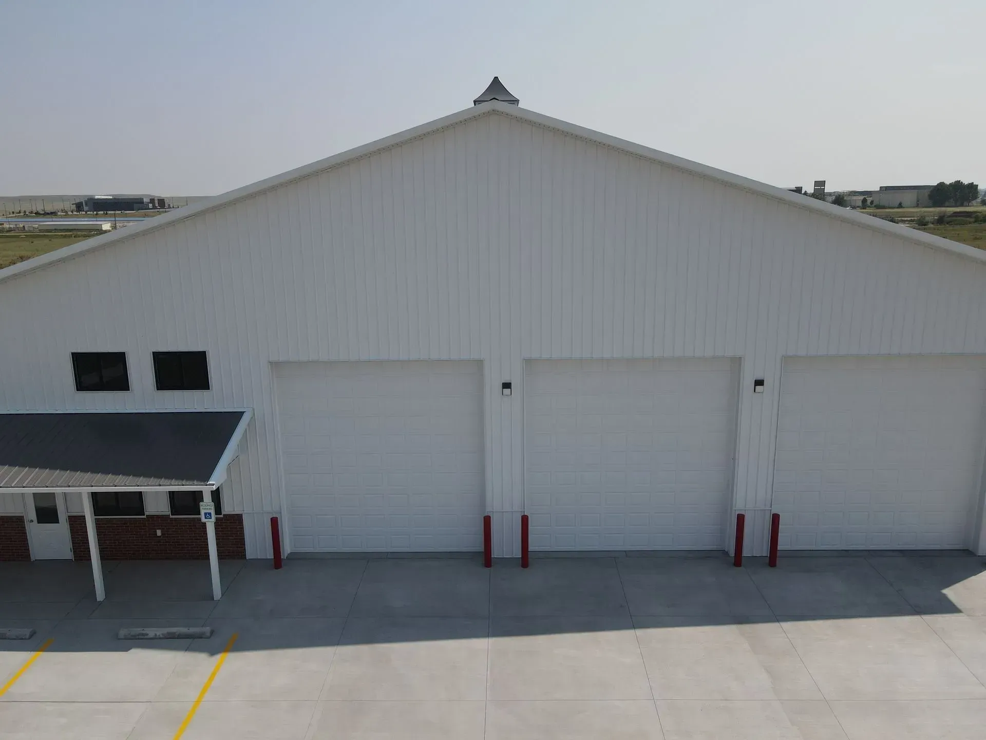 White warehouse building with three garage doors. Black awning over a smaller structure.