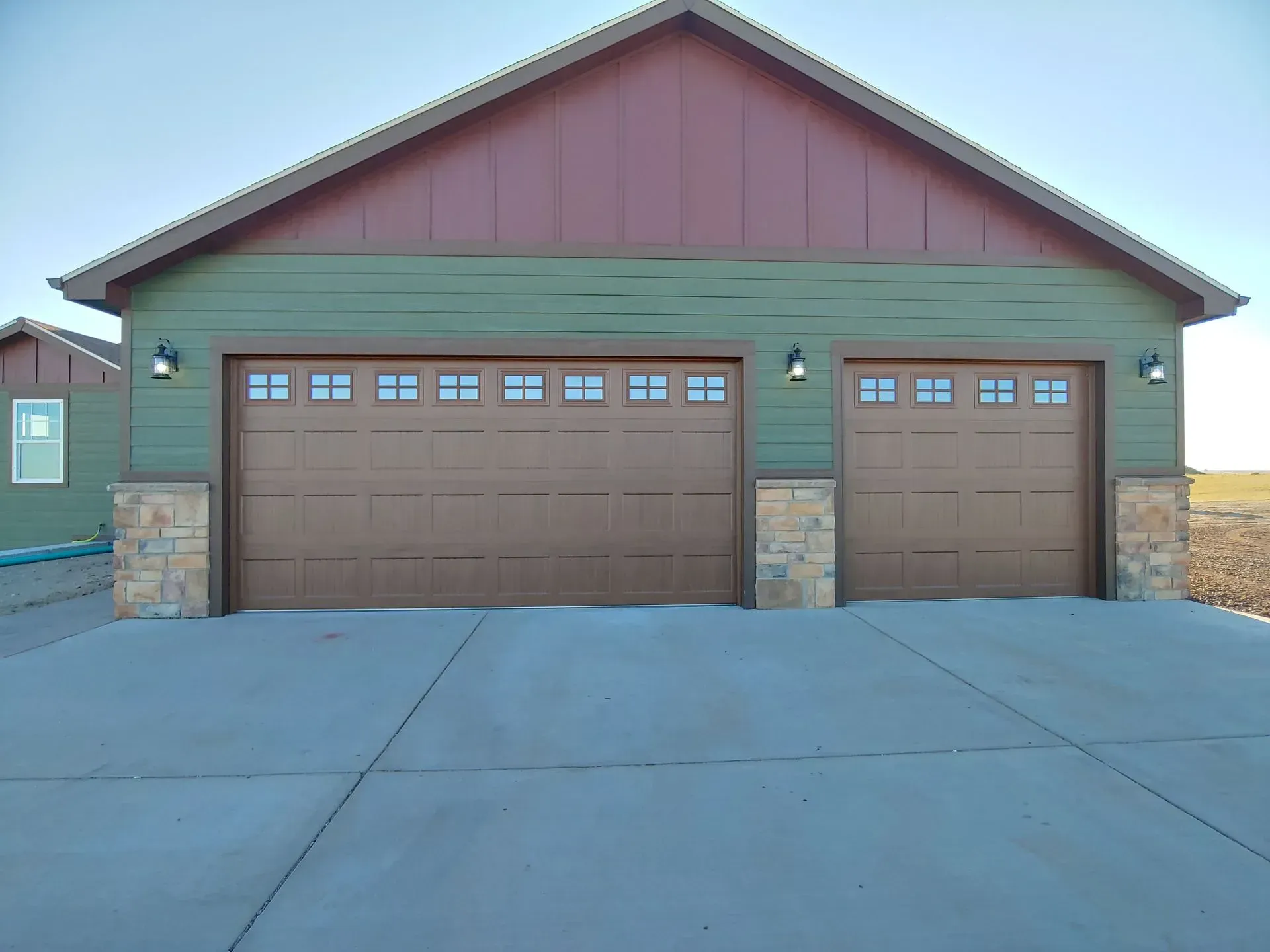 Two-car garage with green siding and brown garage doors, set against a blue sky.