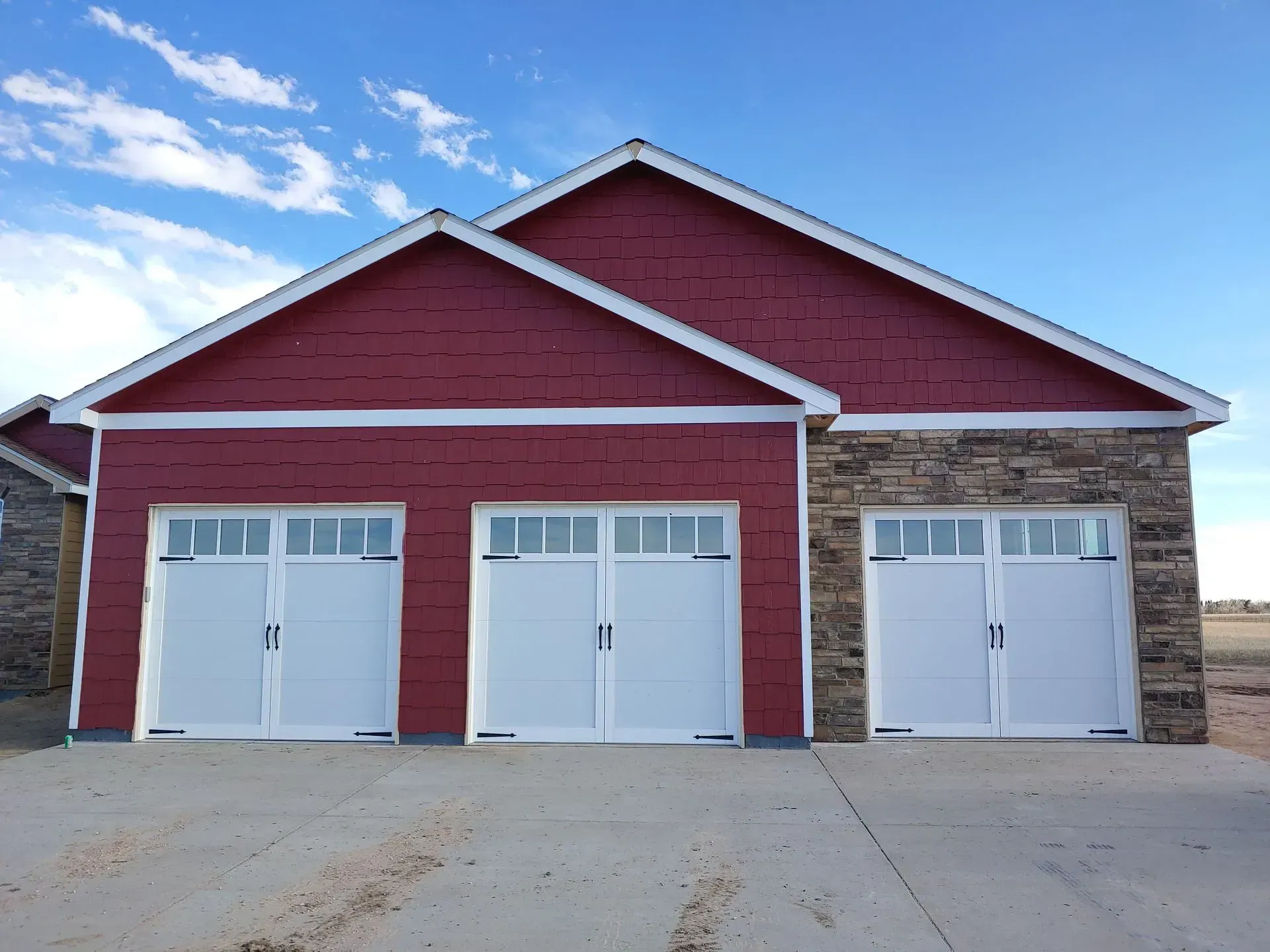 Three-car garage with white doors, red siding, and a stone facade section under a blue sky.