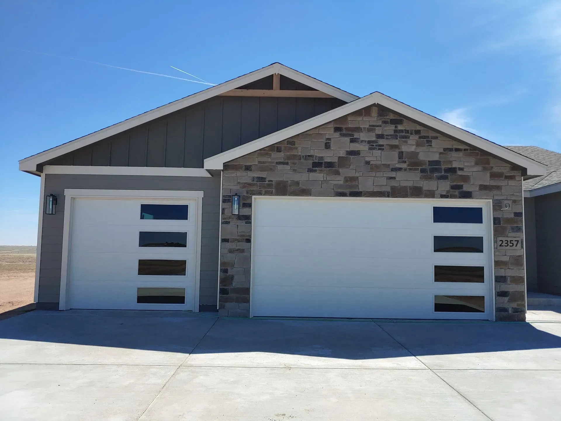Modern house with two white garage doors and stone facade under a blue sky.