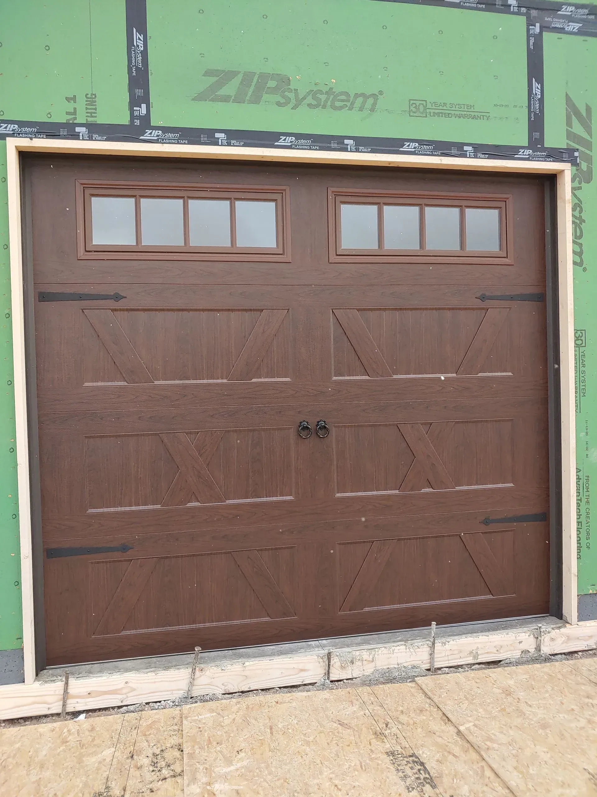 Brown garage door with windows, installed on a house under construction.