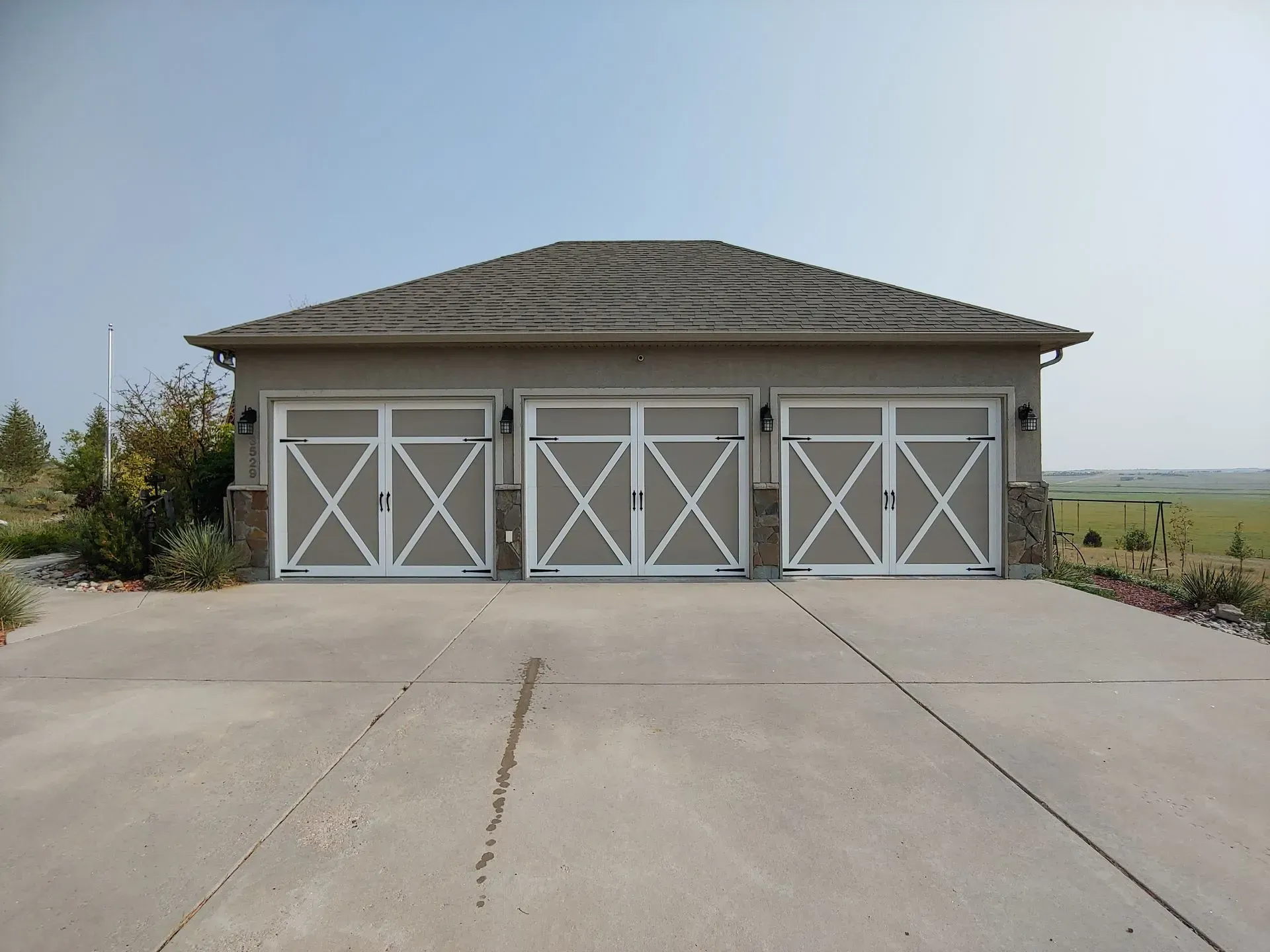 Three-car garage with beige doors, white trim, and a concrete driveway under a clear sky.
