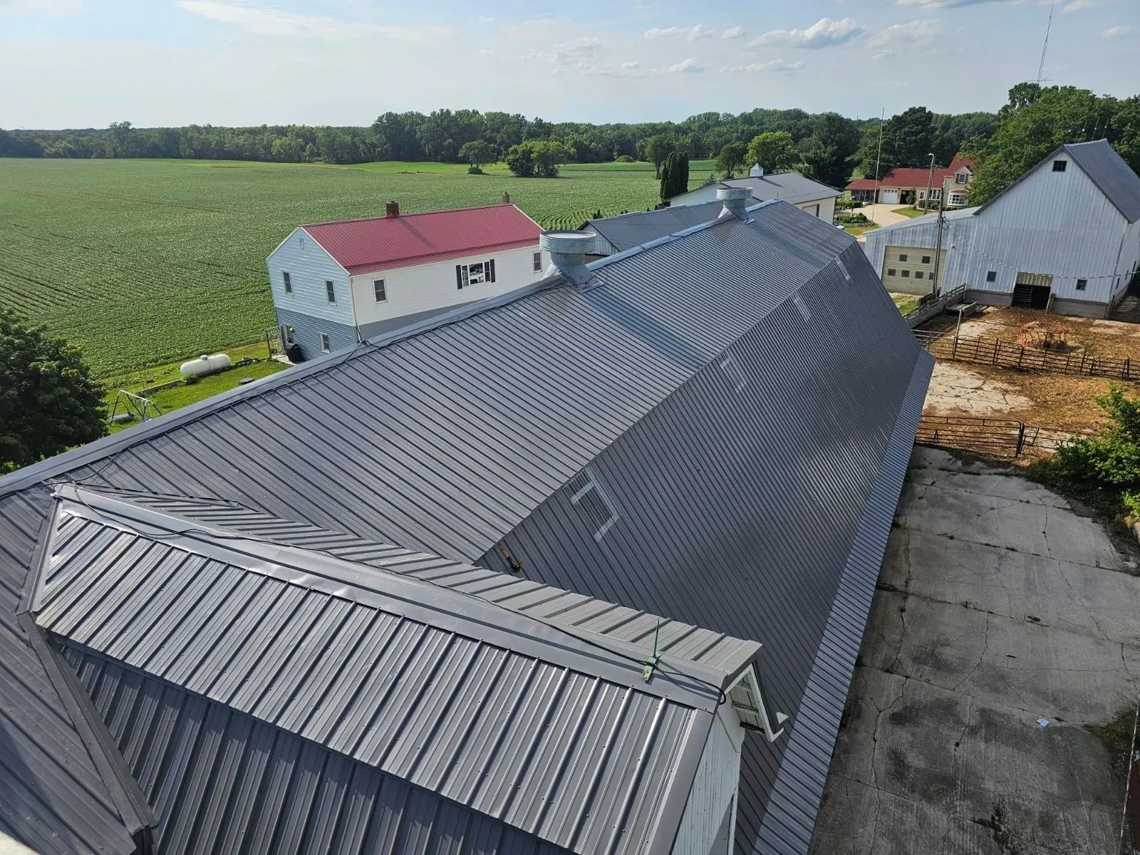 Gray metal-roofed barn beside green fields and neighboring houses on a rural property