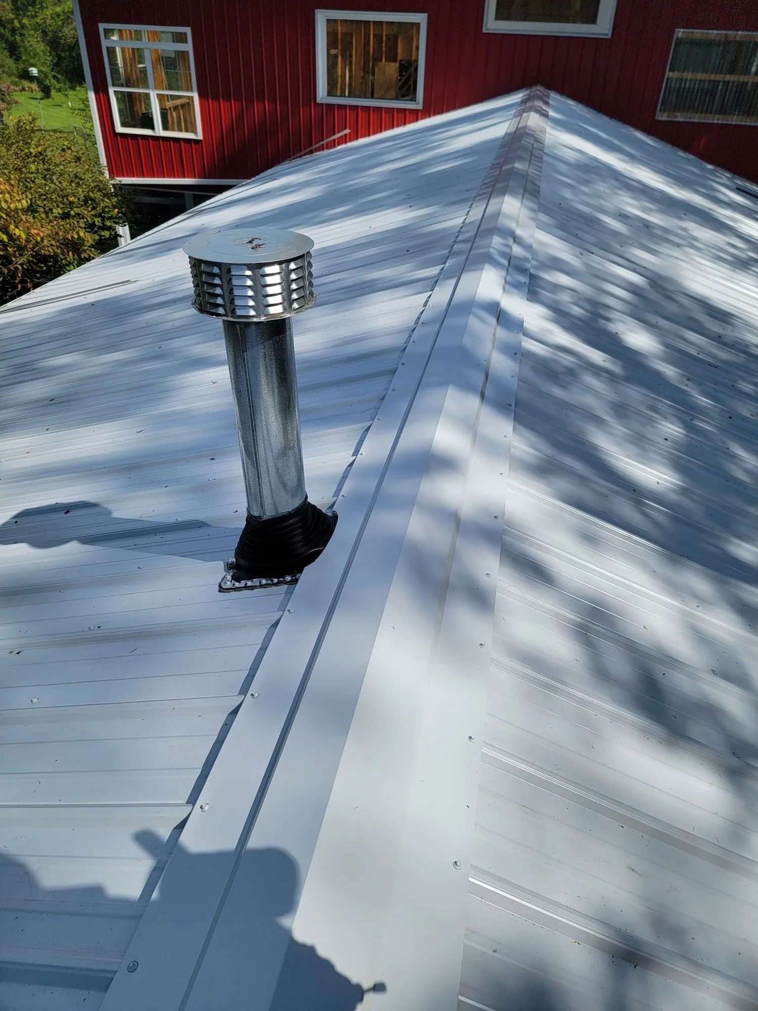 White metal roof with a chimney vent beside a red building with windows.