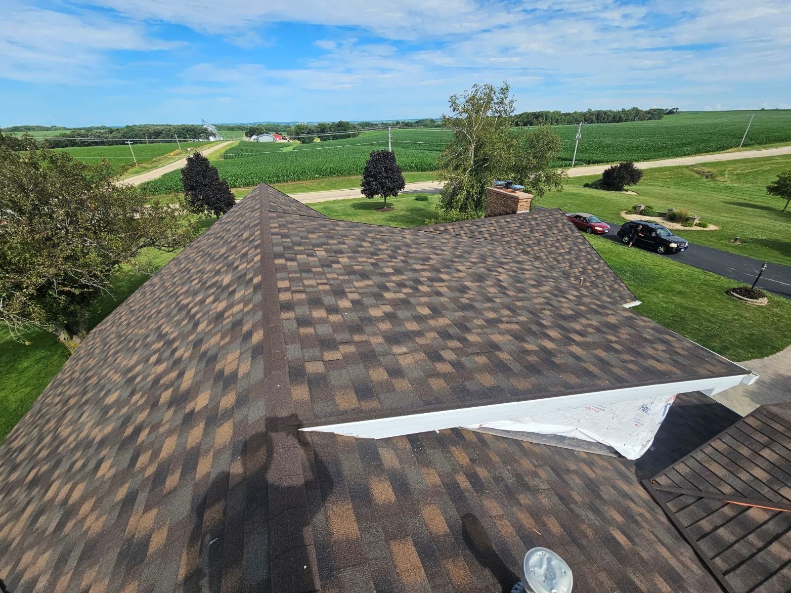 Rooftop view over green fields, trees, and a rural road under a clear sky.