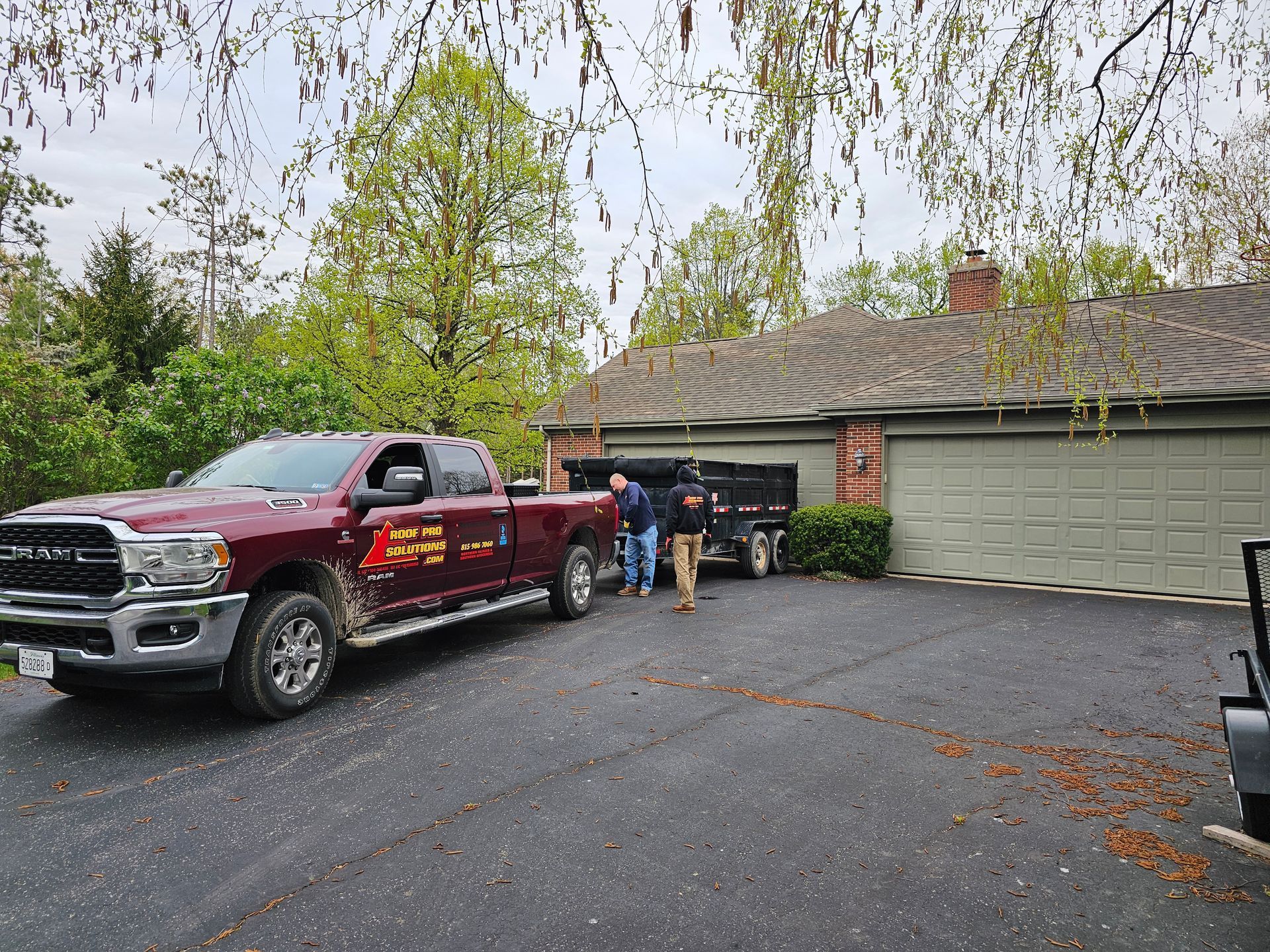 Red pickup truck parked in a driveway beside a garage, with two people near the house and trees overhead.