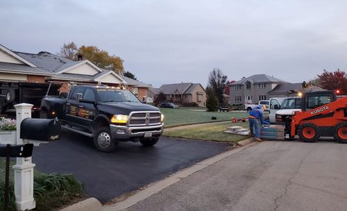 Black pickup truck and orange tow truck on a suburban street, loading equipment near a house