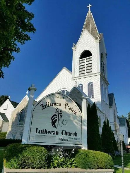 White Lutheran church with tall steeple and sign under a blue sky