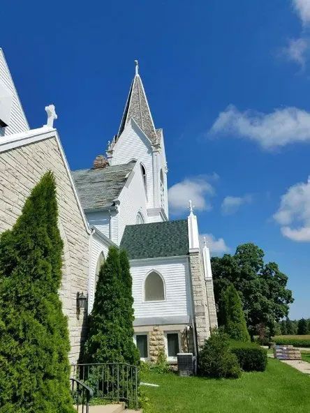 White church with a tall steeple beside a green lawn under a bright blue sky.