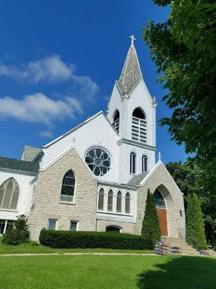 White stone church with tall steeple and stained-glass windows under a blue sky