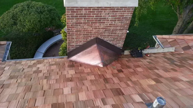 Rooftop shingles and a brick chimney with a copper flashing surround.